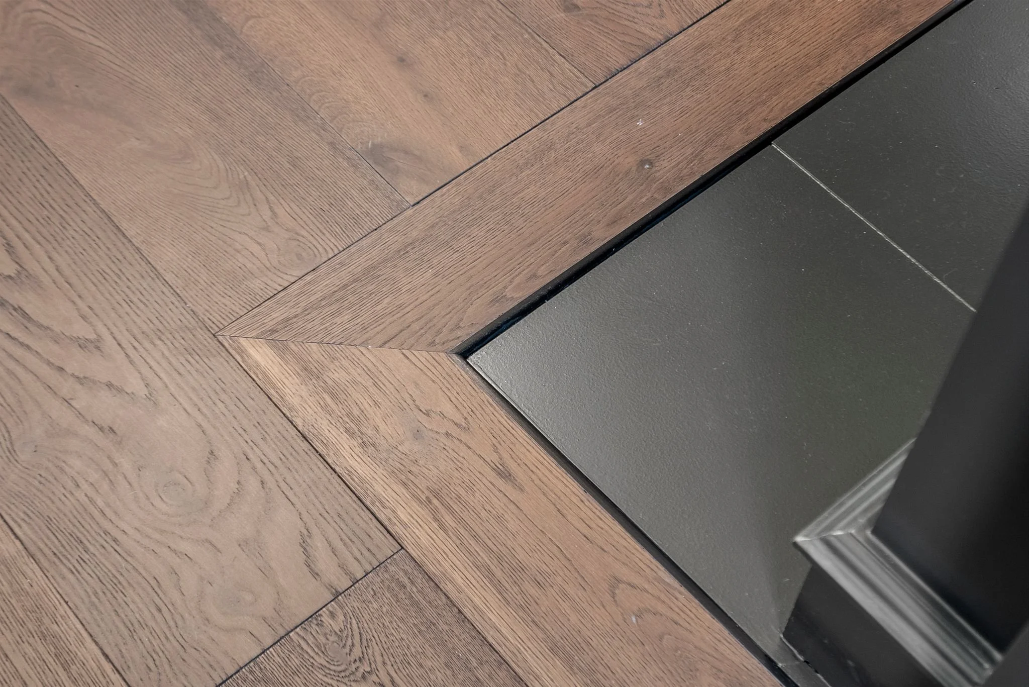 Detail of herringbone oak flooring meeting a black fireplace hearth