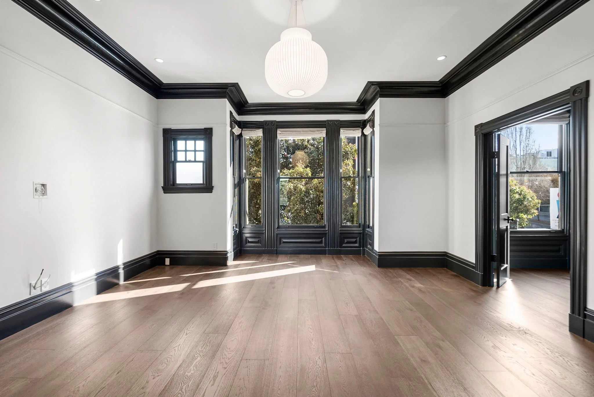 Bright front parlor with black-trimmed bay window, black crown molding and white globe pendant