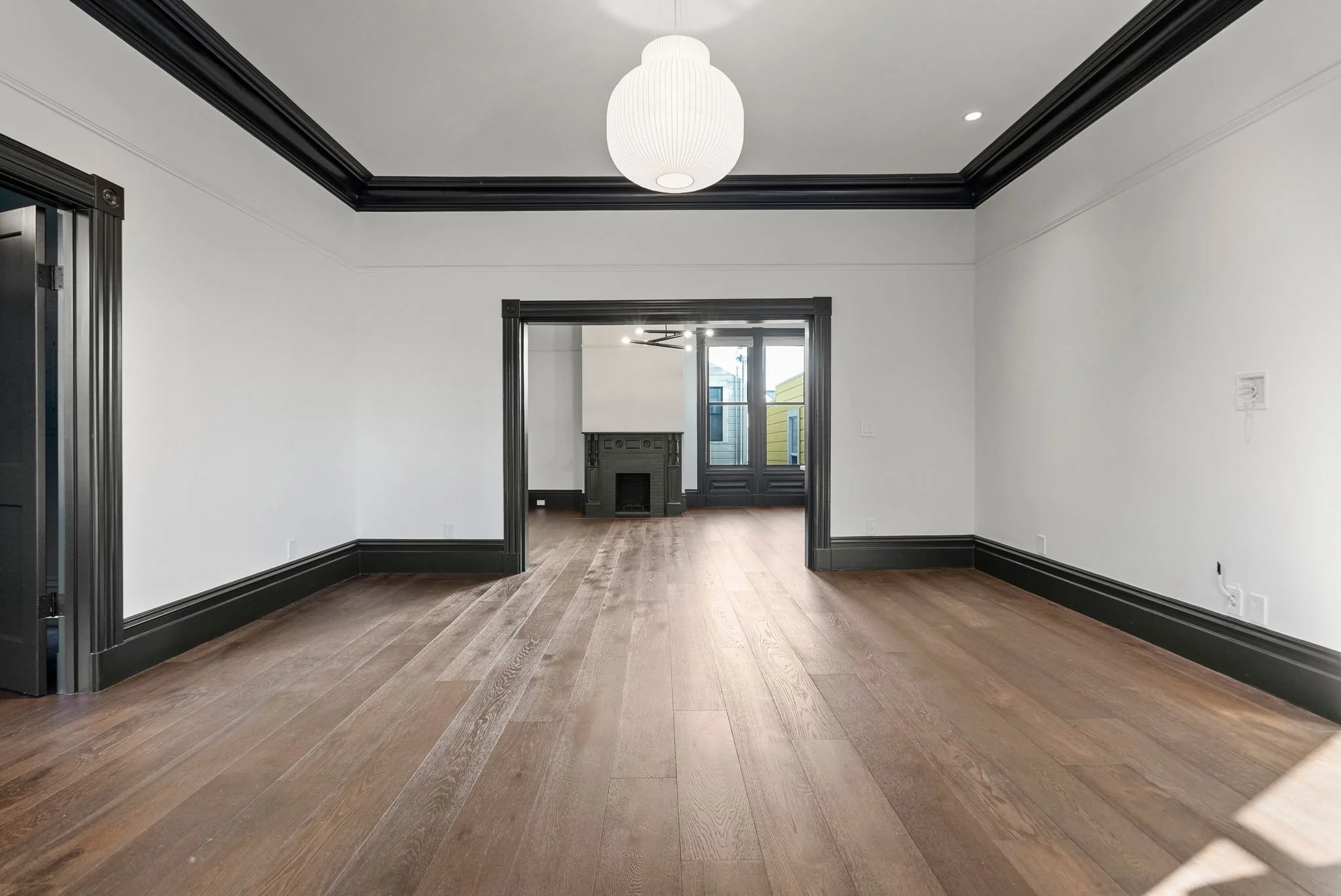 Open parlor looking through cased opening toward fireplace, with oak floors and black picture rail