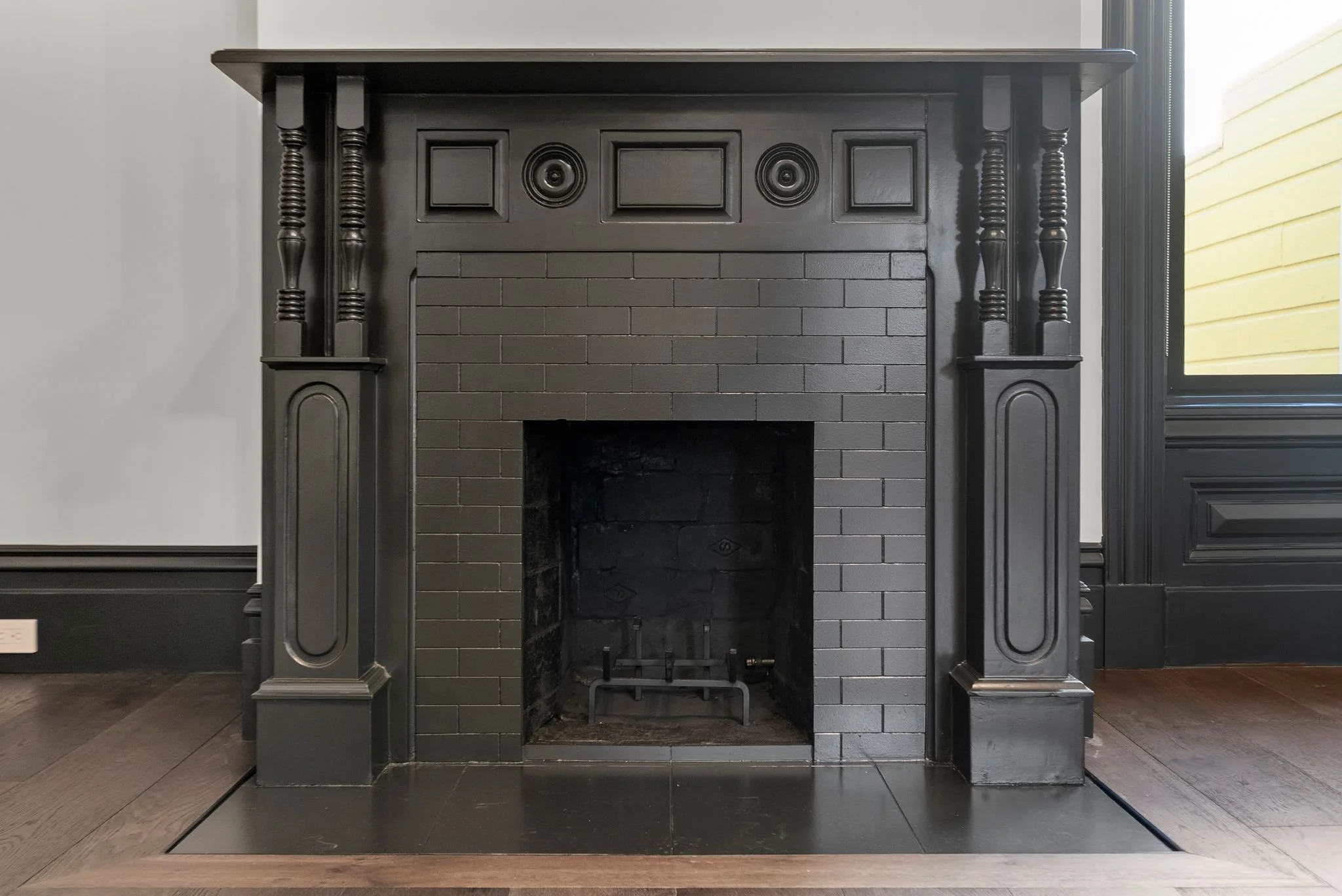 Restored Victorian fireplace with black-painted carved mantel and black brick surround