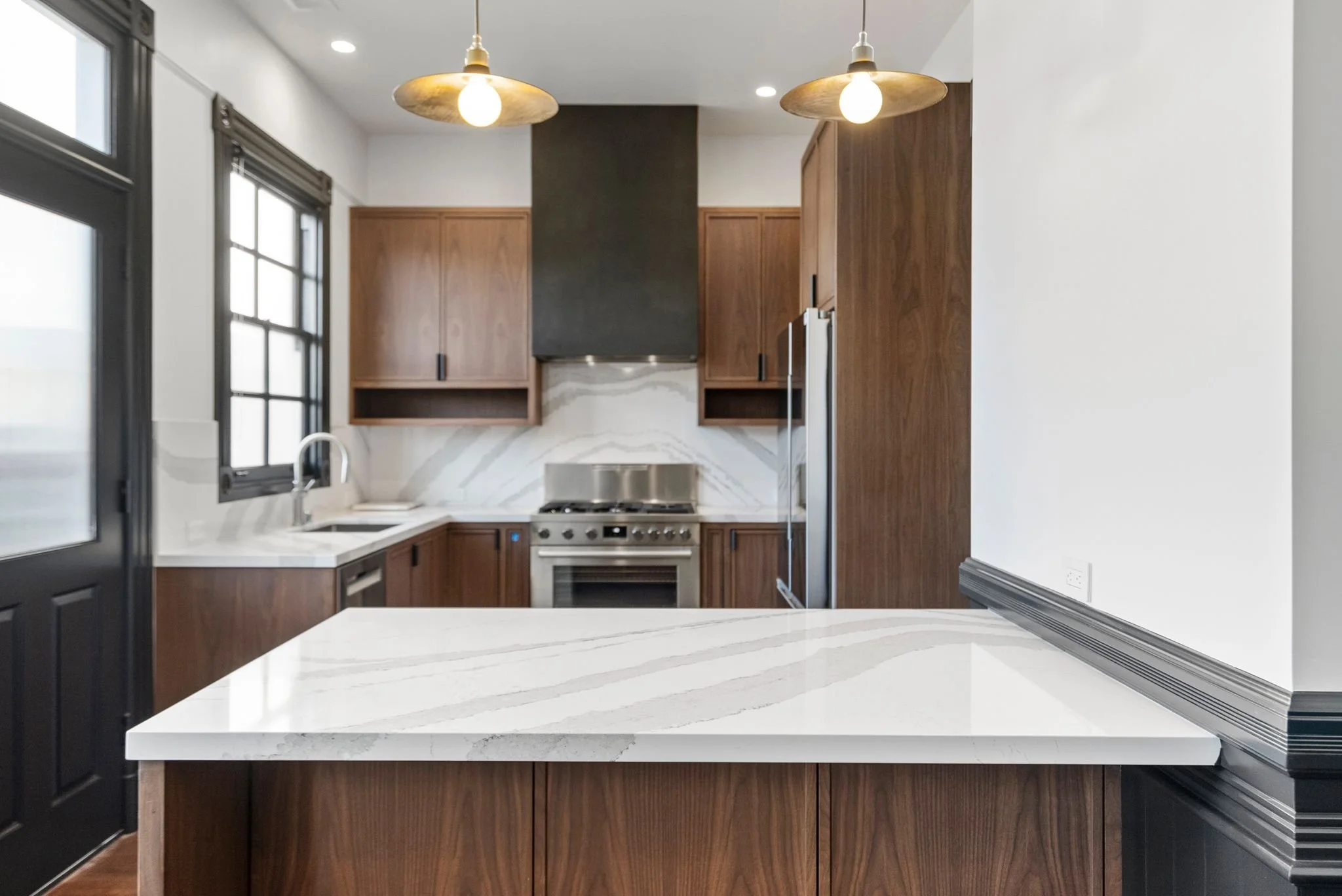 Kitchen with quartz waterfall island, walnut cabinets, black range hood and brass pendant lights
