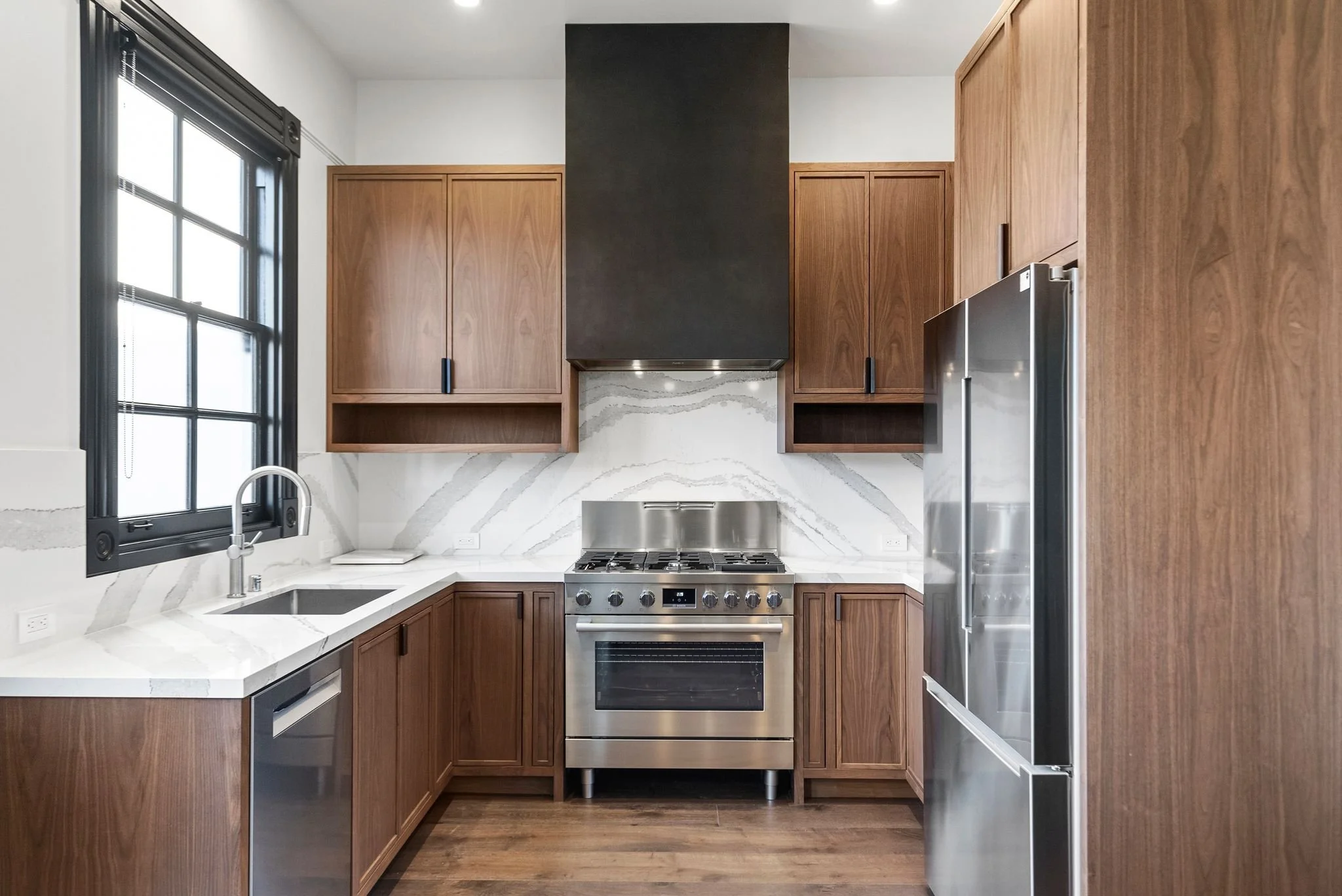 Kitchen with walnut cabinetry, stainless steel range and refrigerator, white quartz backsplash and black window trim