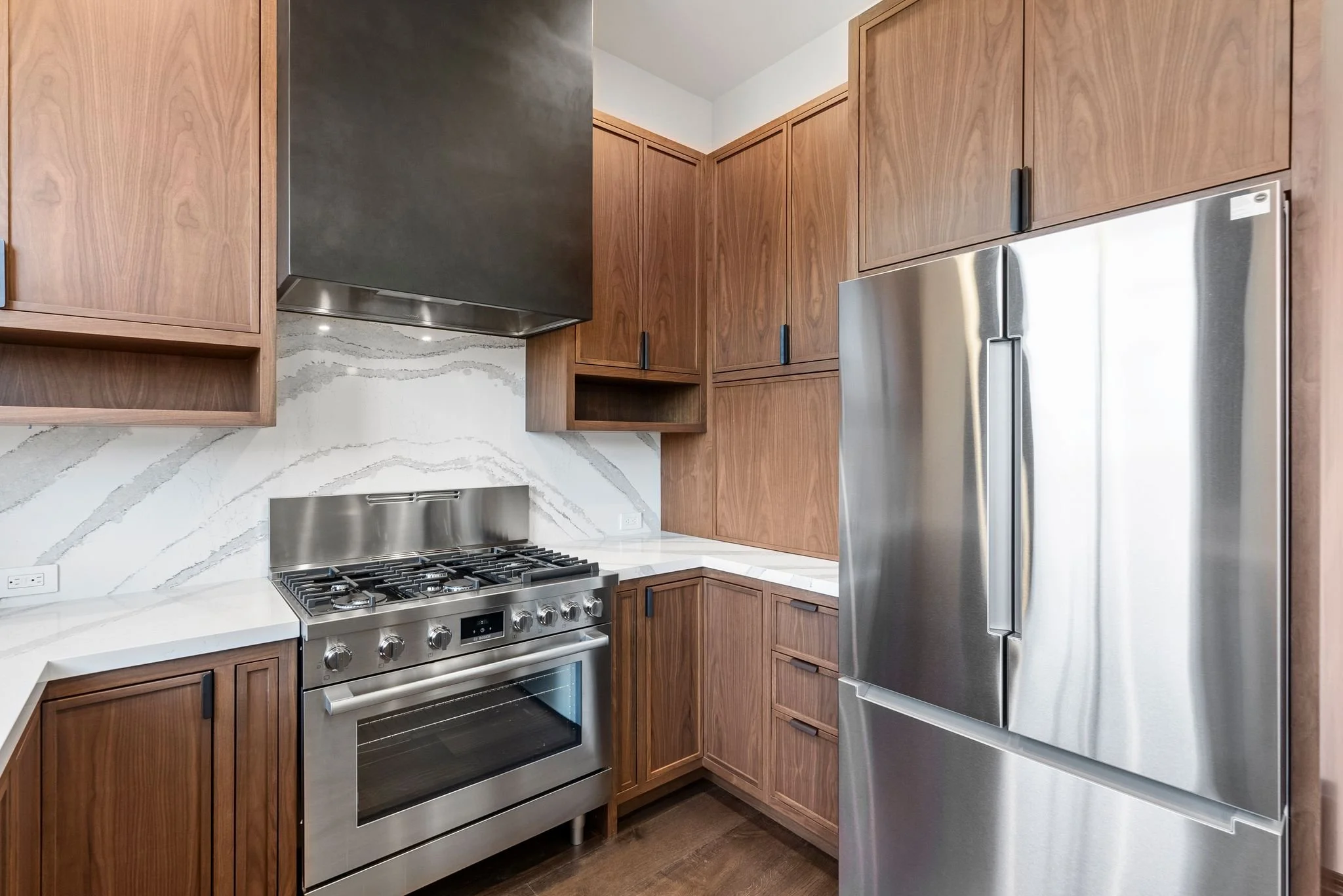 Kitchen cooking wall with stainless range, black hood and walnut upper cabinets
