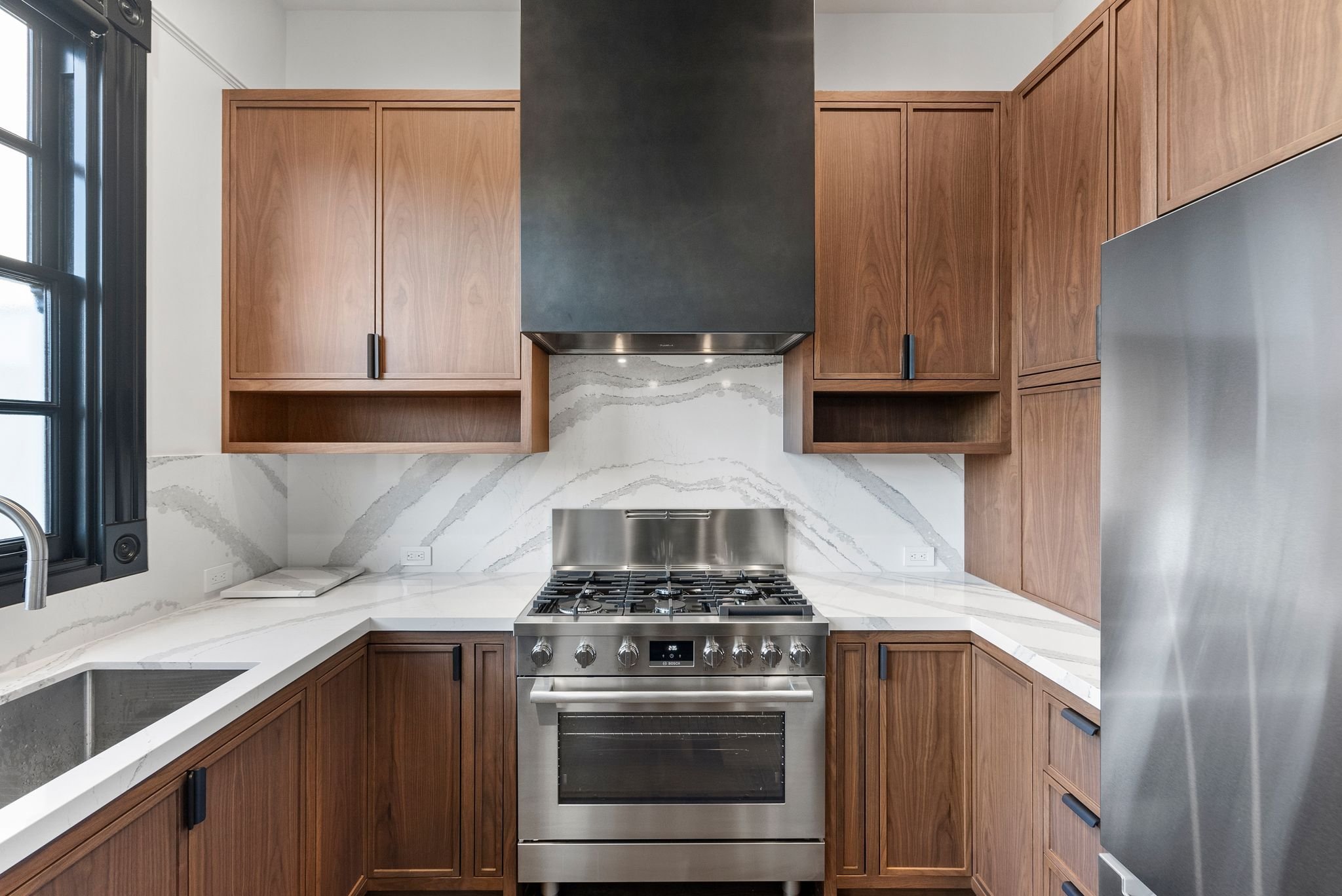 Kitchen with black-trimmed window over sink, walnut cabinets and stainless appliances
