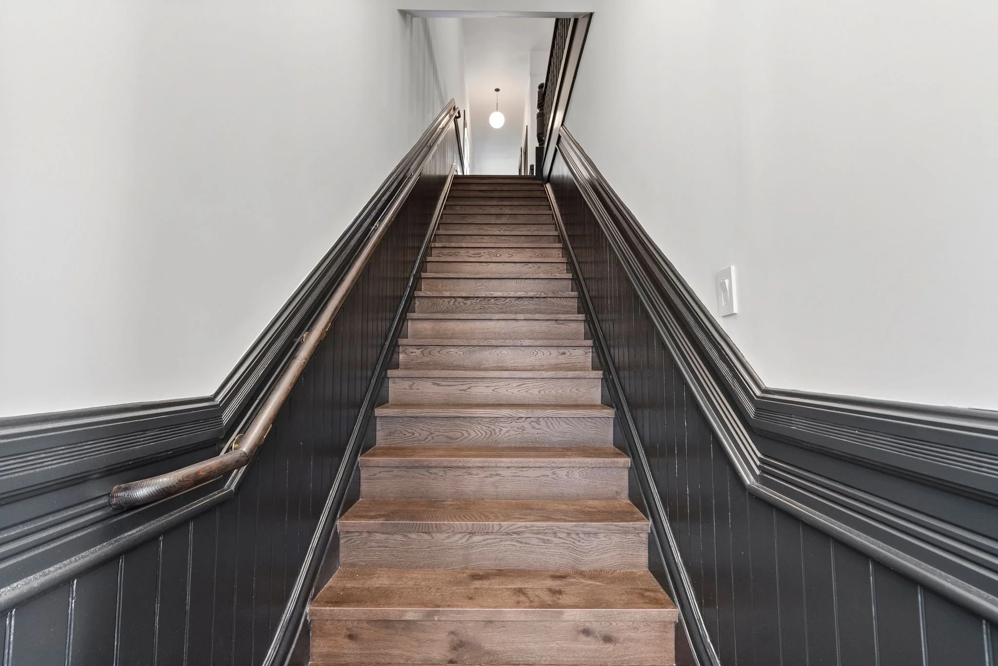 Staircase with oak treads, black-painted risers, black wainscoting and wood handrail