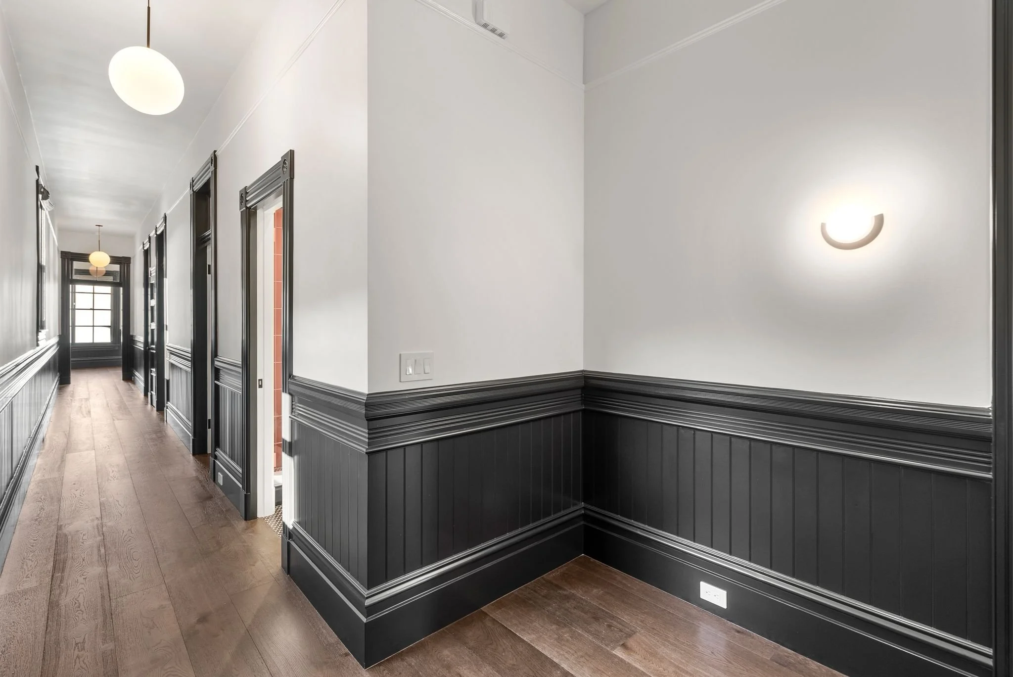Long hallway with black beadboard wainscoting, oak floors and white globe pendant