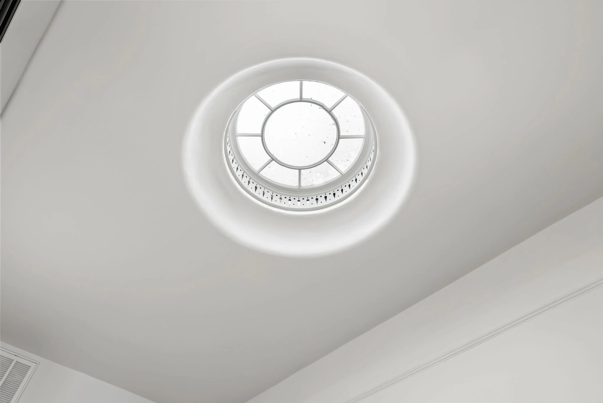 Circular skylight well in a white ceiling with wall vent