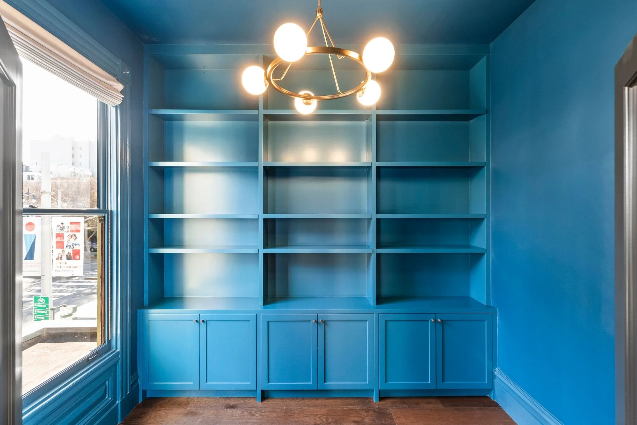 Built-in bookcase and window wall painted deep teal blue with brass chandelier