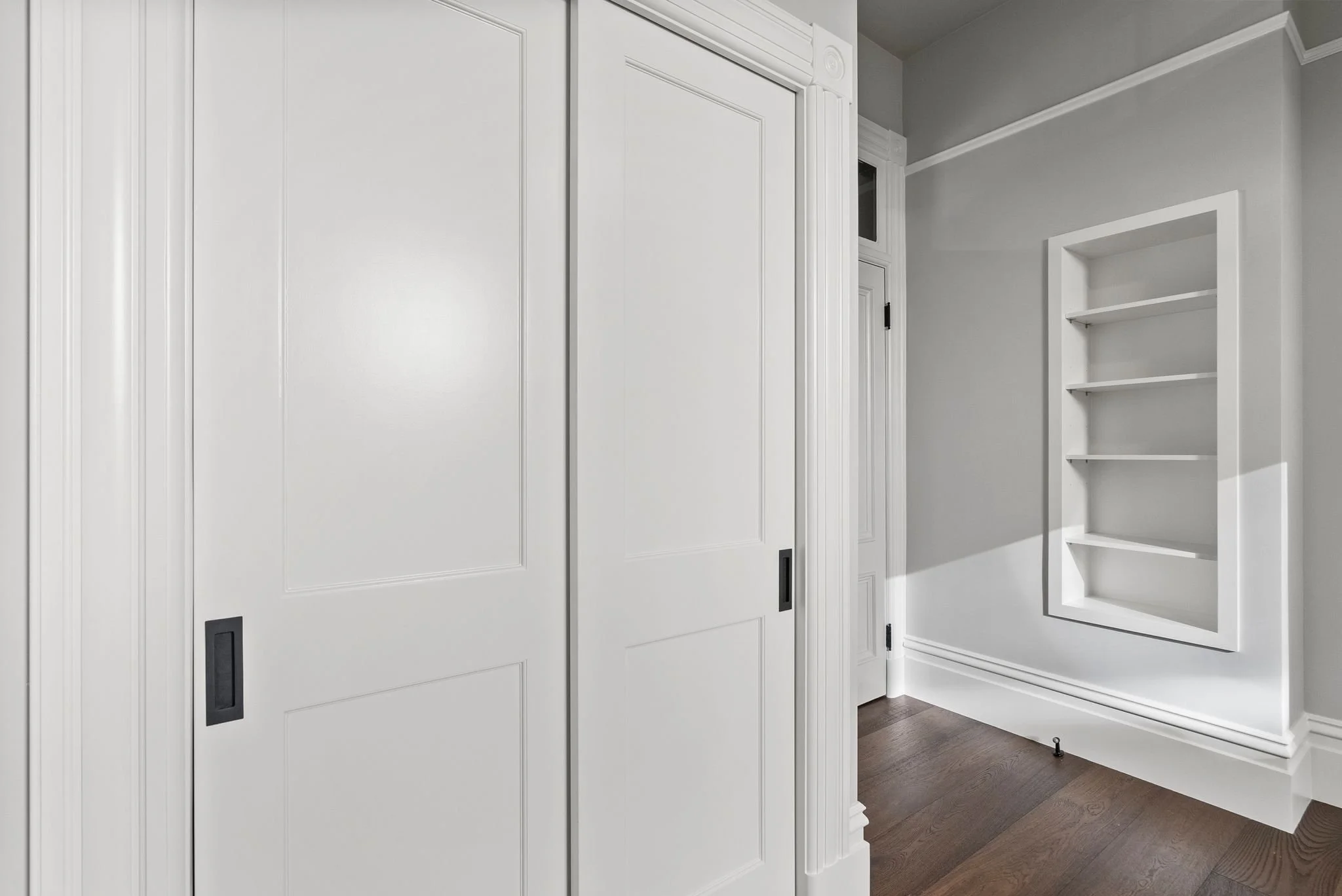 Hallway with white paneled doors, sliding closet door and built-in shelving niche
