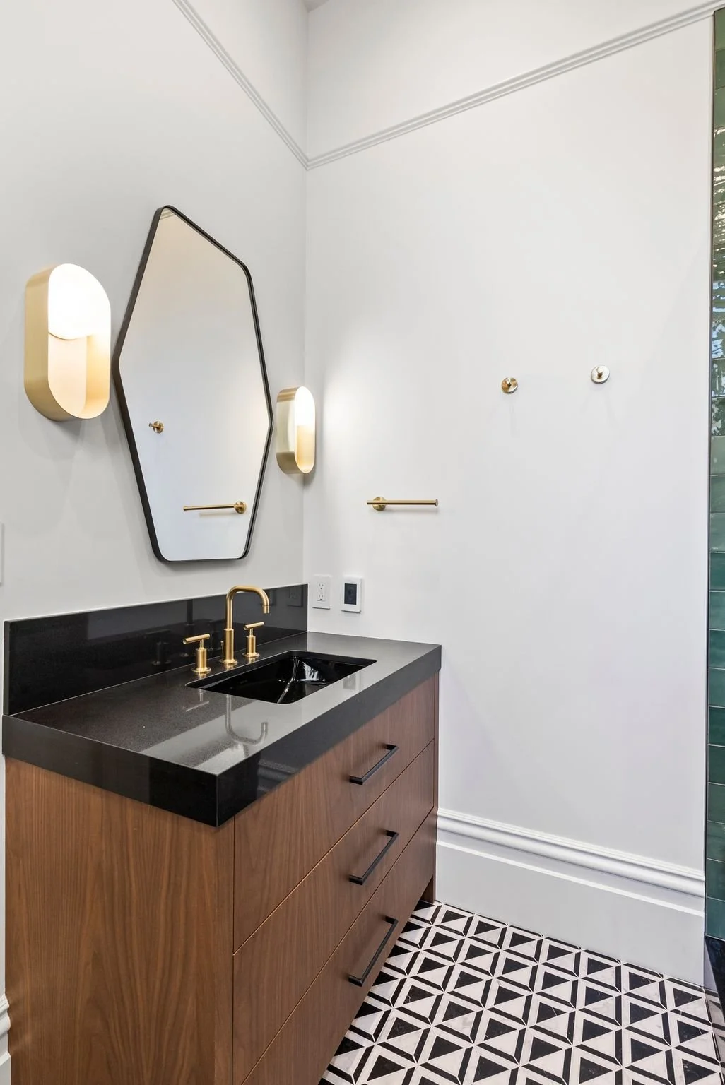 Bathroom vanity with walnut cabinet, black countertop, brass faucet, geometric mirror and brass sconces
