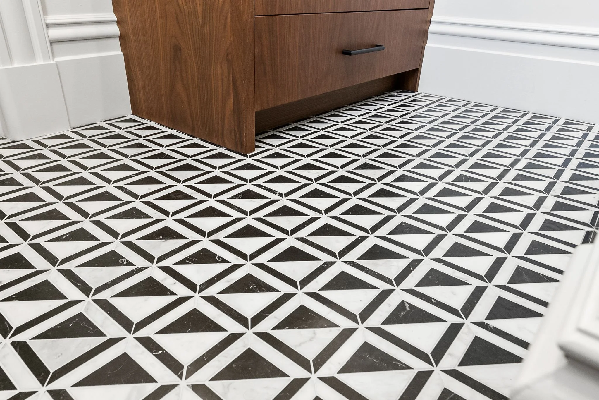Black and white geometric patterned floor tile beside walnut vanity