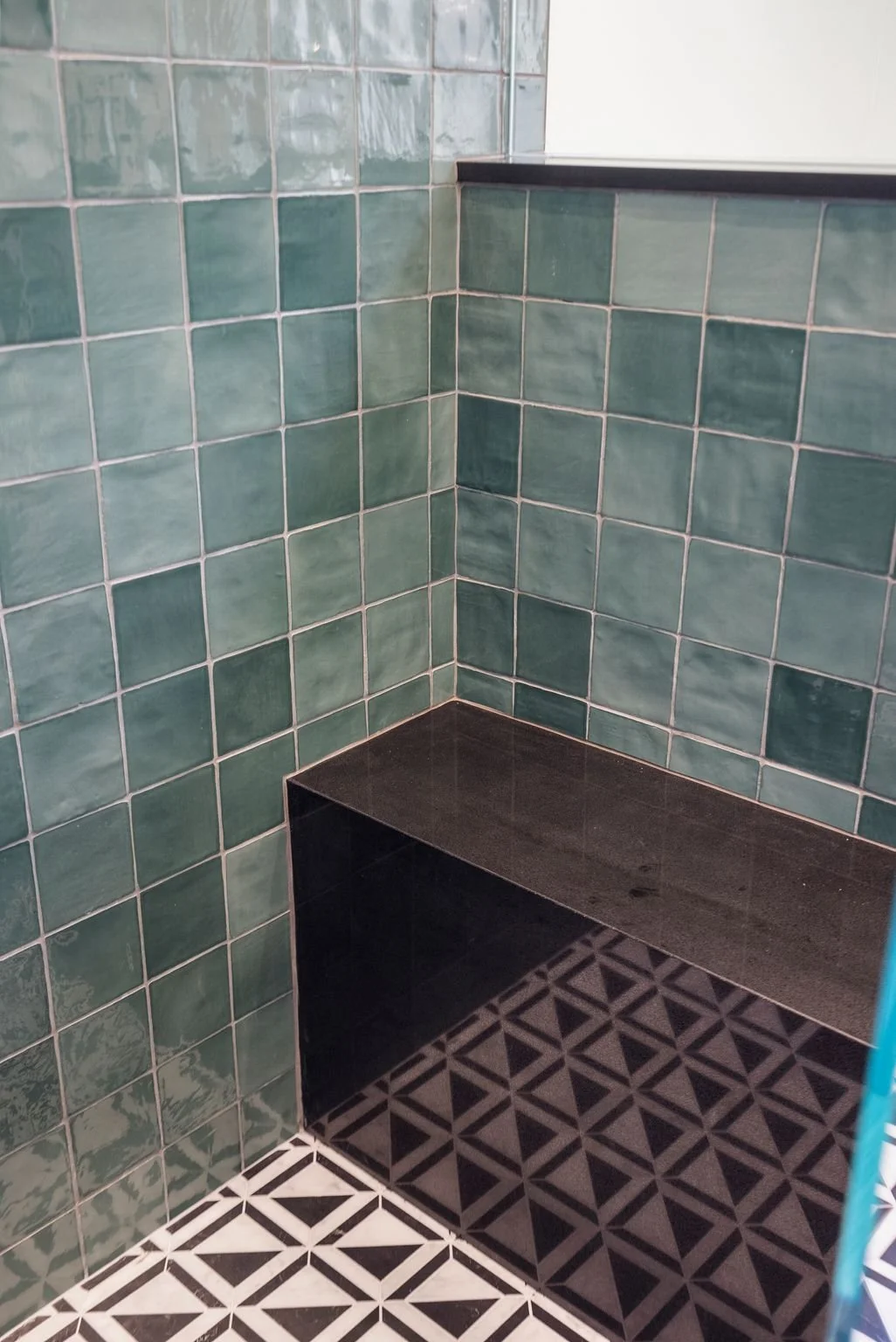 Green tiled shower with built-in black bench and patterned tile floor