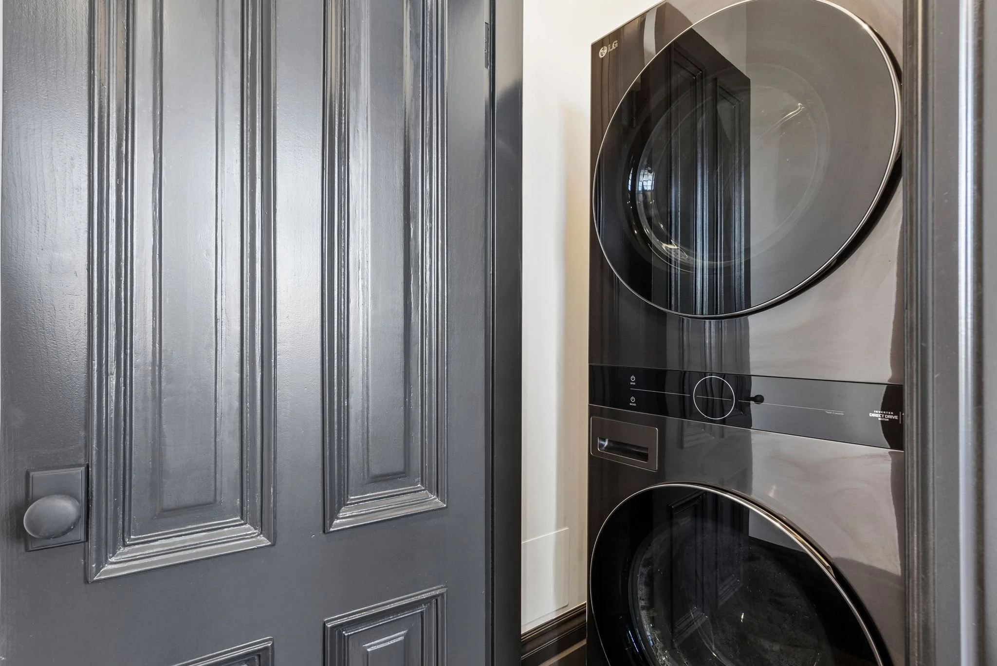 Laundry closet with stacked washer and dryer behind black paneled door
