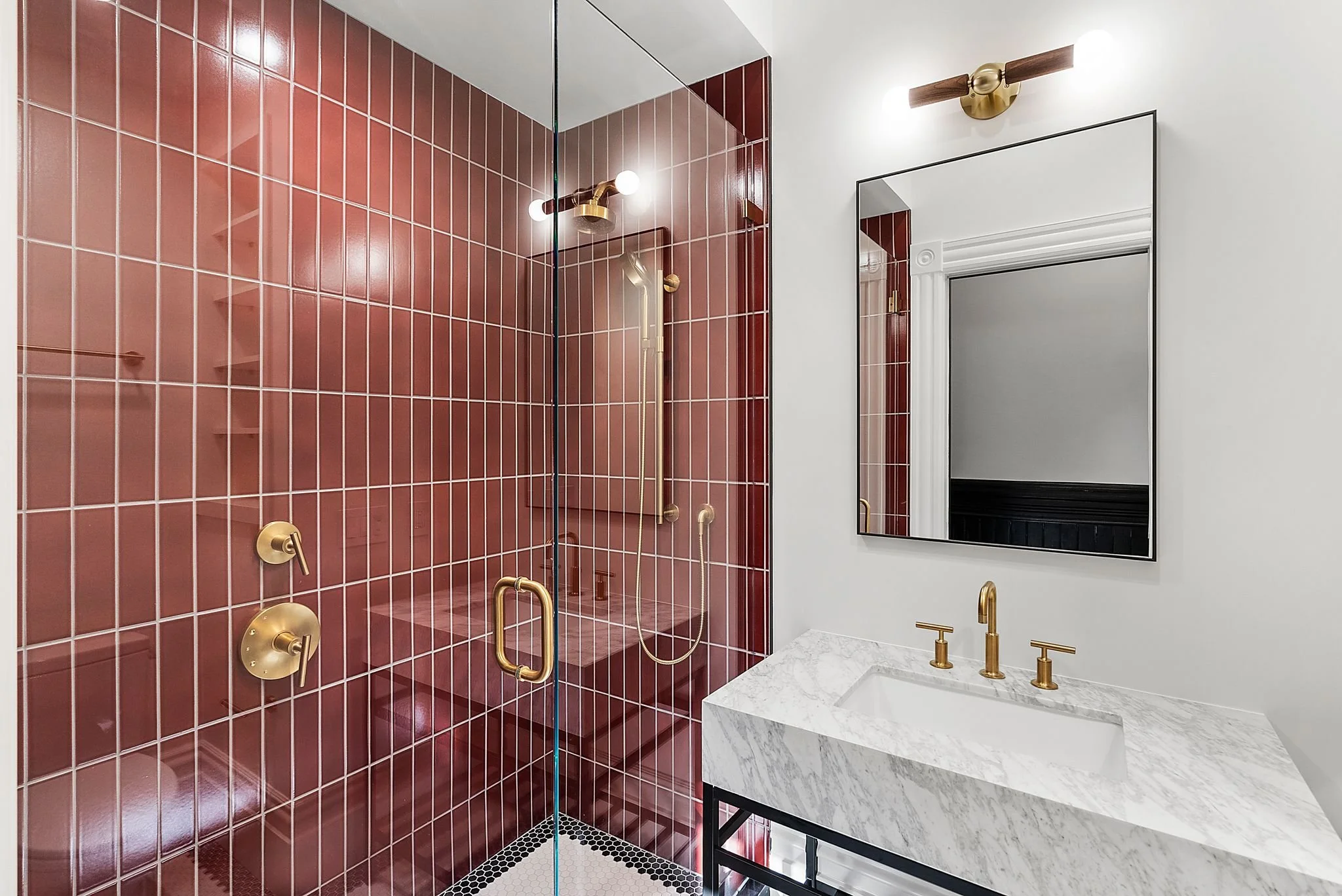 Bathroom with oxblood red vertical tile shower, marble console sink and brass fixtures