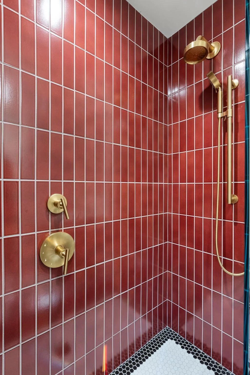 Glossy red stacked tile shower with brass rain head, hand shower and hexagon tile floor