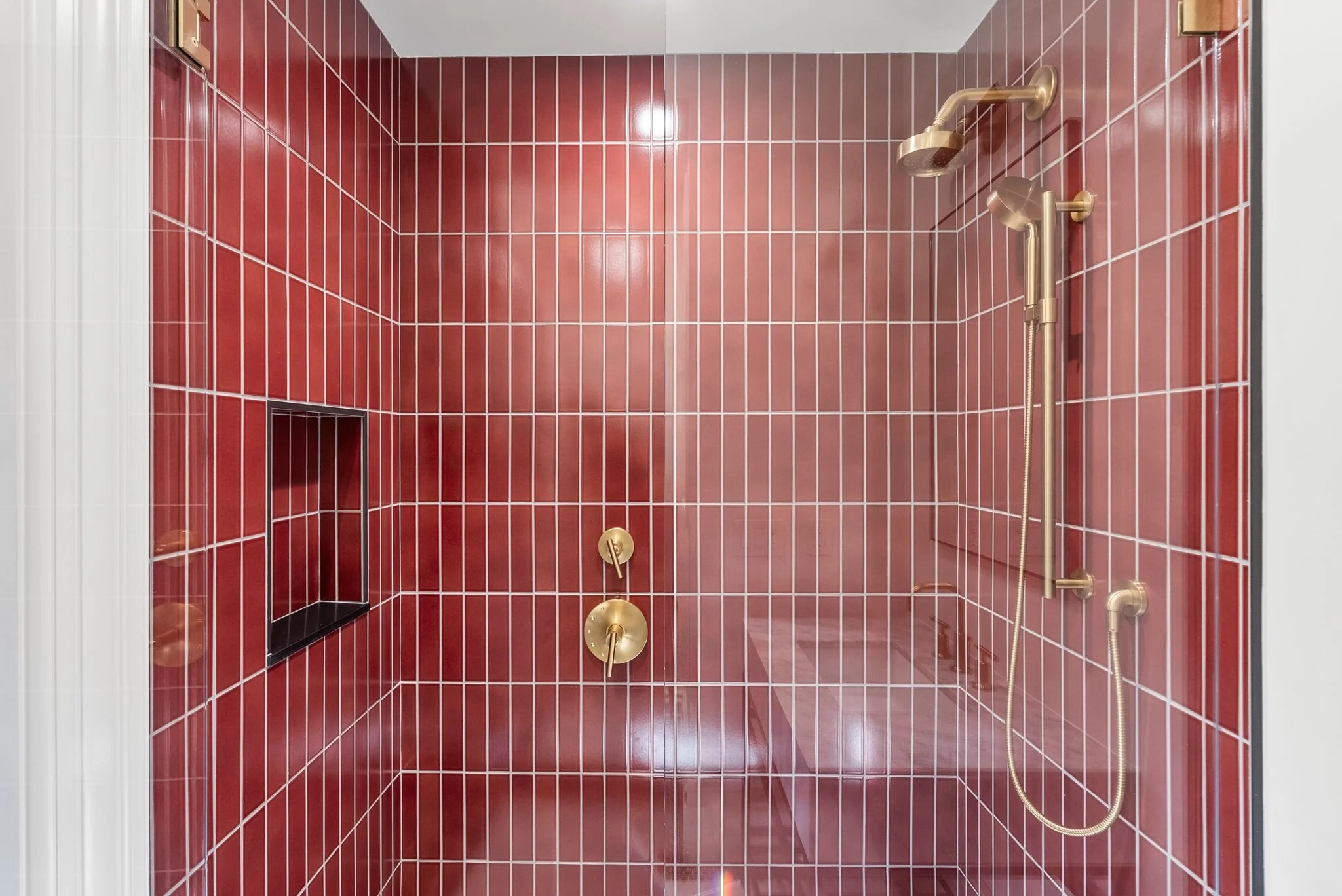 Red tiled walk-in shower with recessed niche and brass shower fixtures