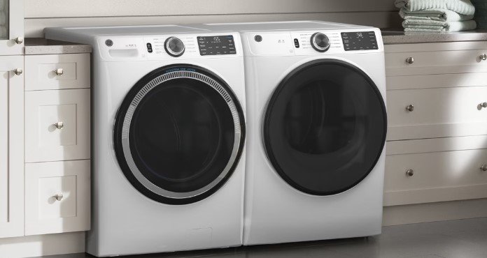 Front view of a white washing machine and dryer set in a laundry room with white cabinetry.