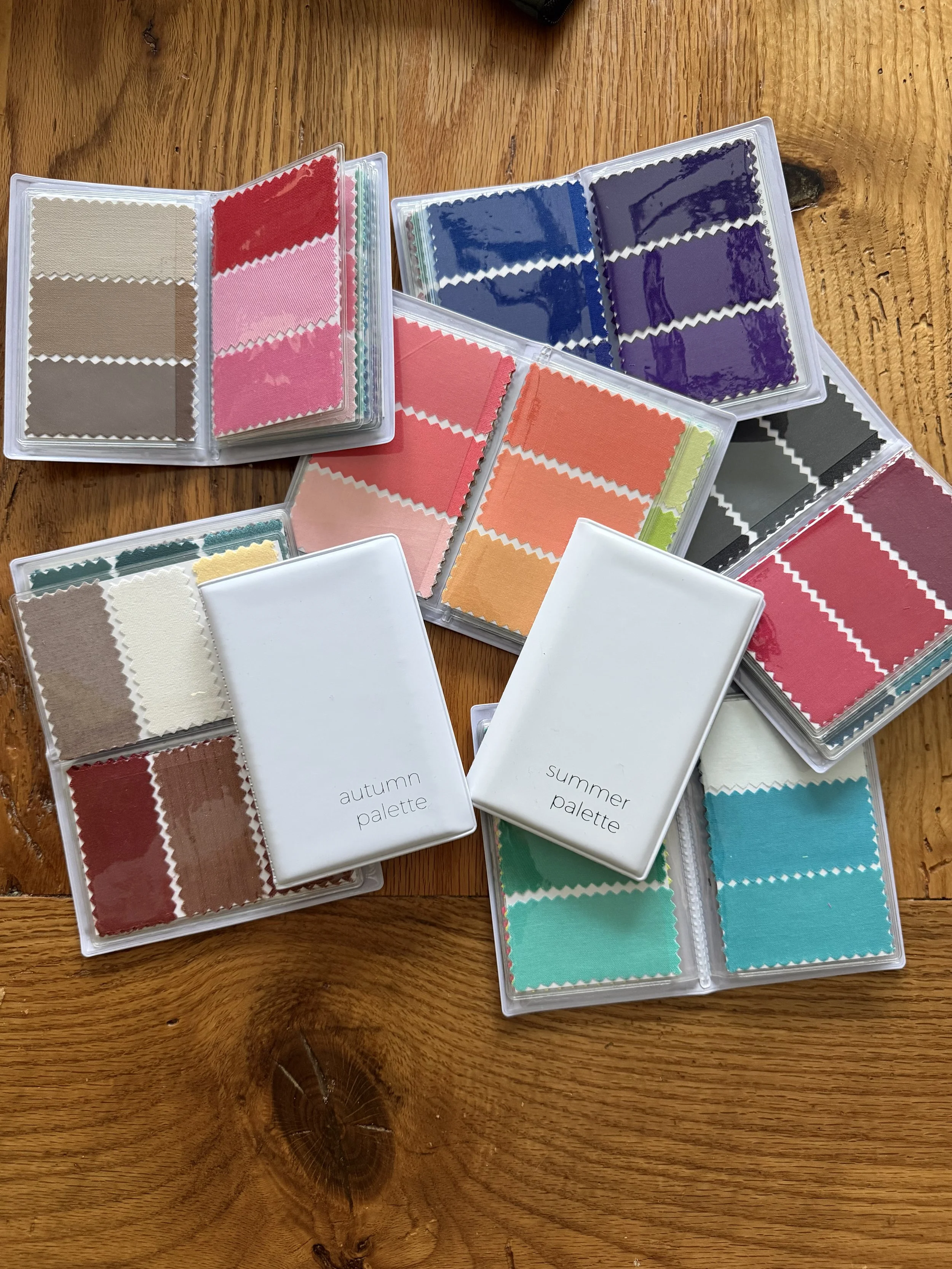 Multiple small fabric swatches in plastic cases, labeled as 'autumn palette' and 'summer palette', arranged on a wooden surface.