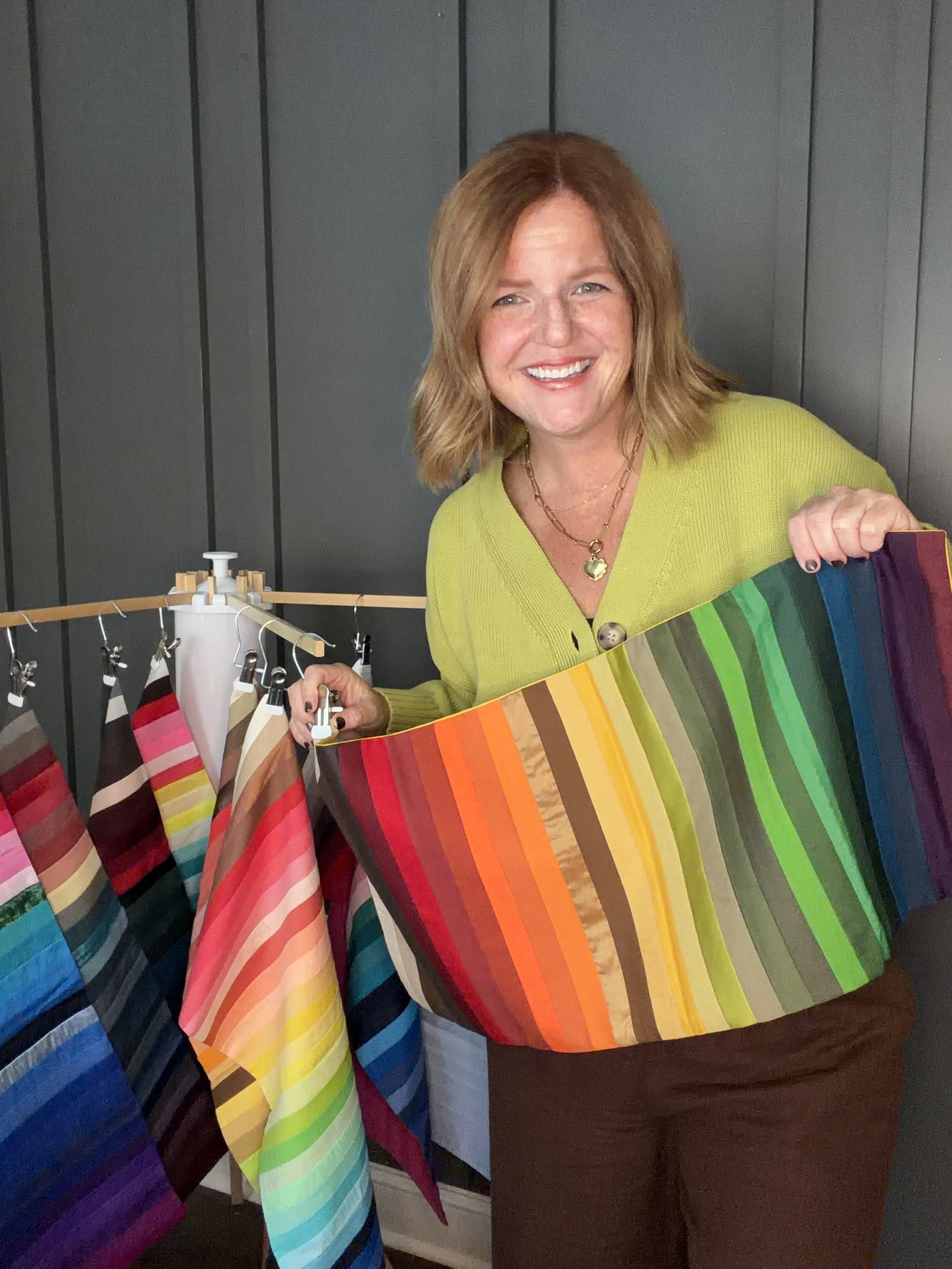 Woman holding a seasonal color palette flag, standing next to a clothing rack with similar  items.