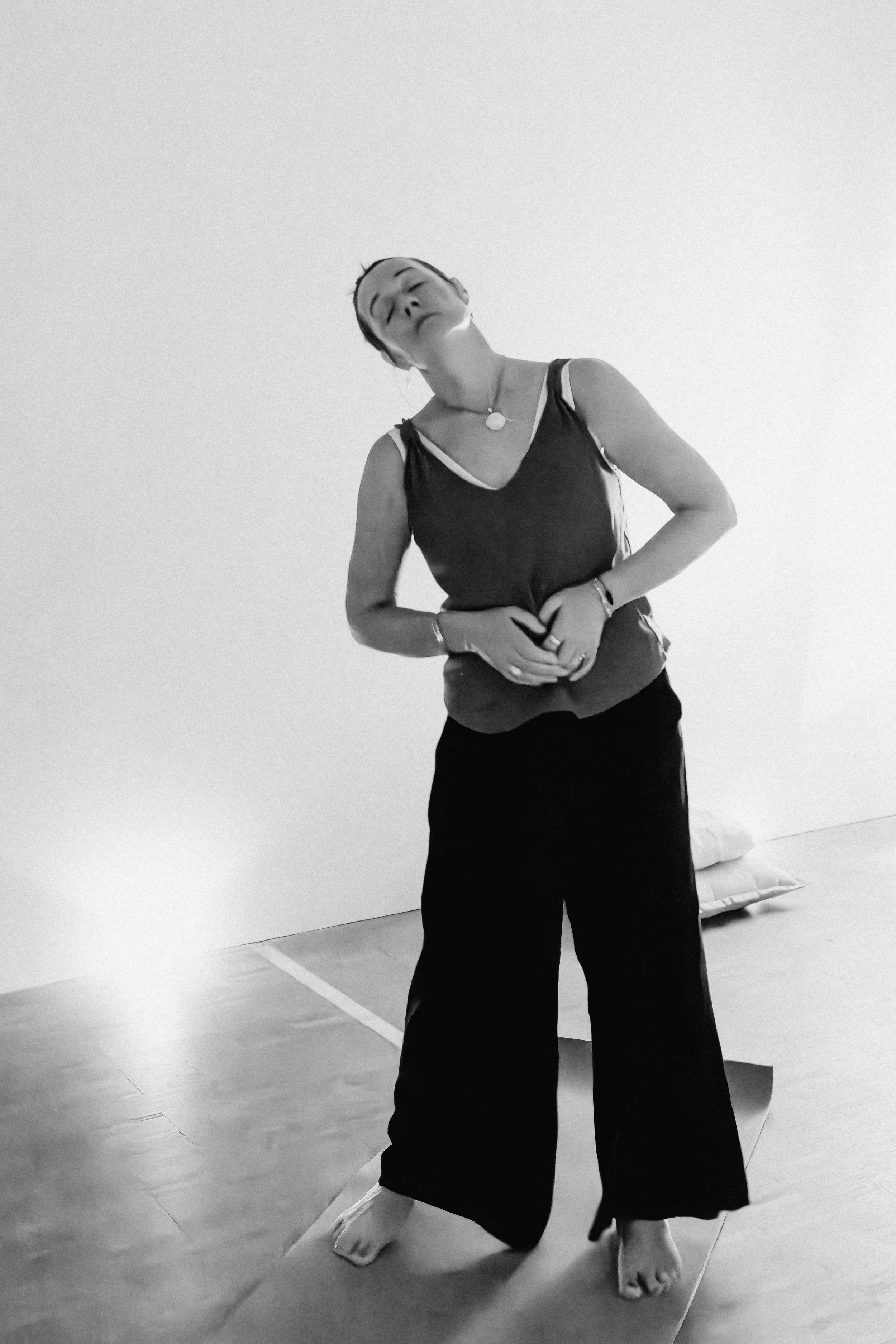 Black-and-white photo of a woman practicing a martial arts pose on a padded mat, with a plain wall in the background.