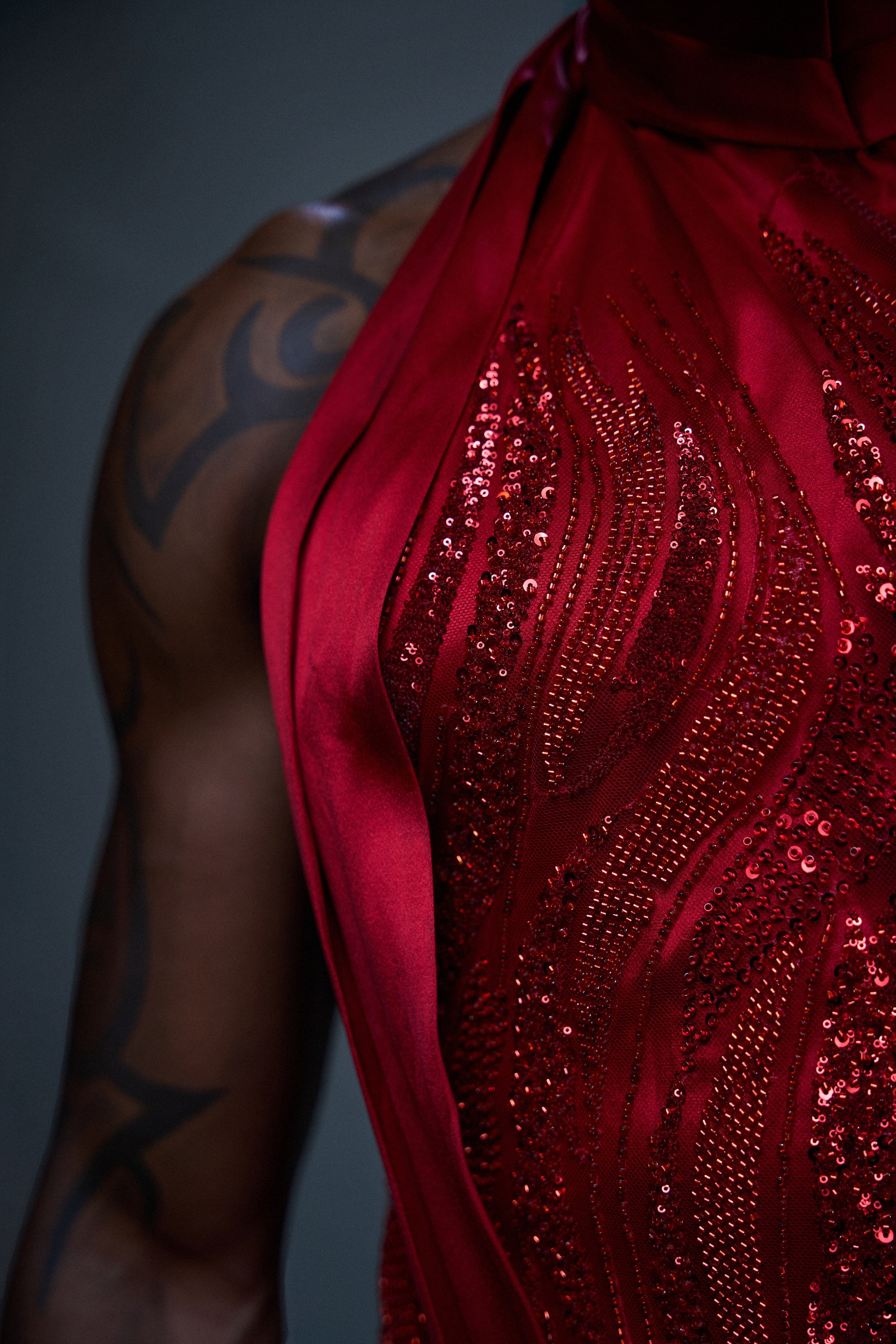 Close-up of a woman wearing a red, sequined, and shiny dress with silver embellishments, exposing her upper arm tattoo.