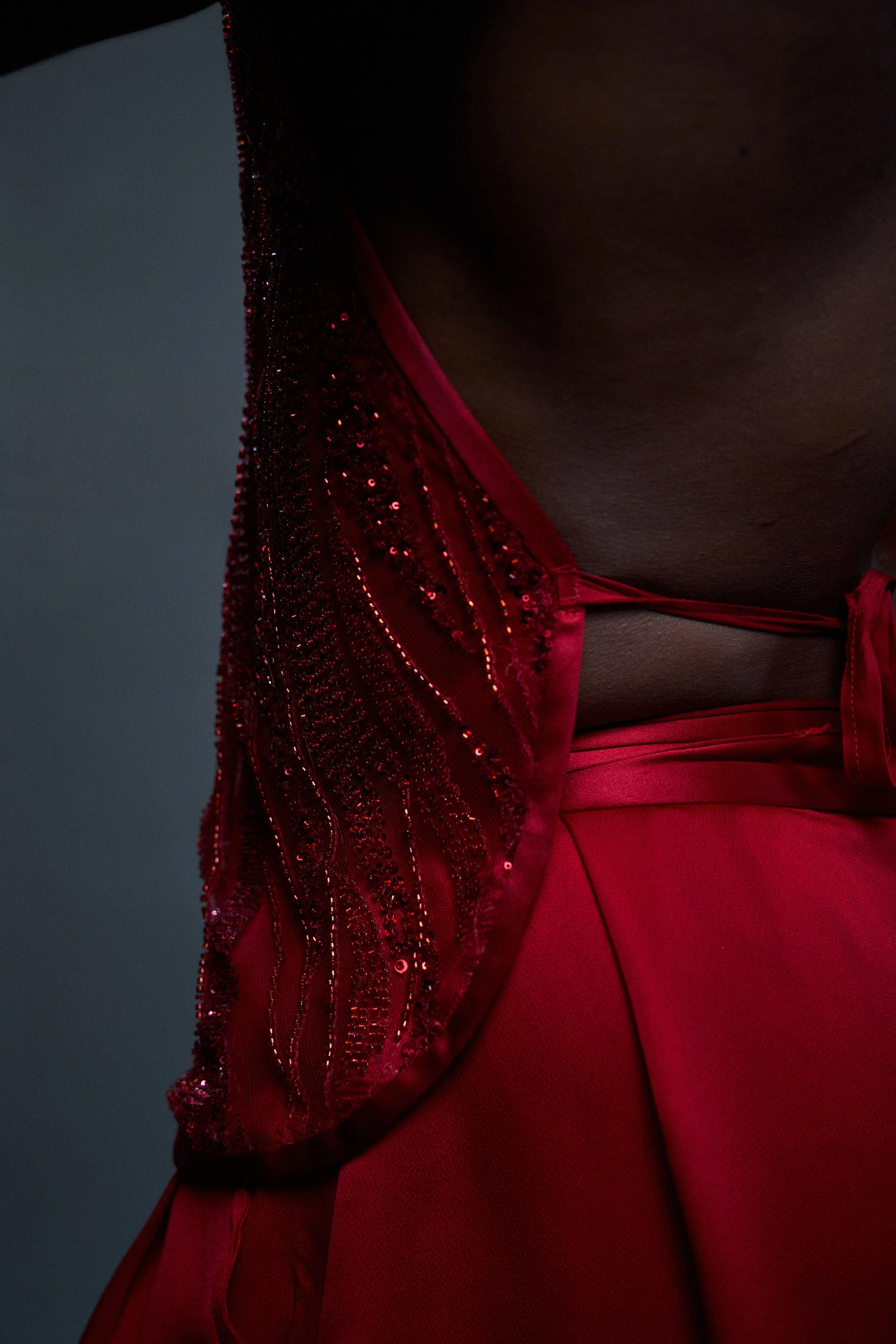 Close-up of a person's torso wearing a red garment with embellishments and a satin finish, against a dark background.