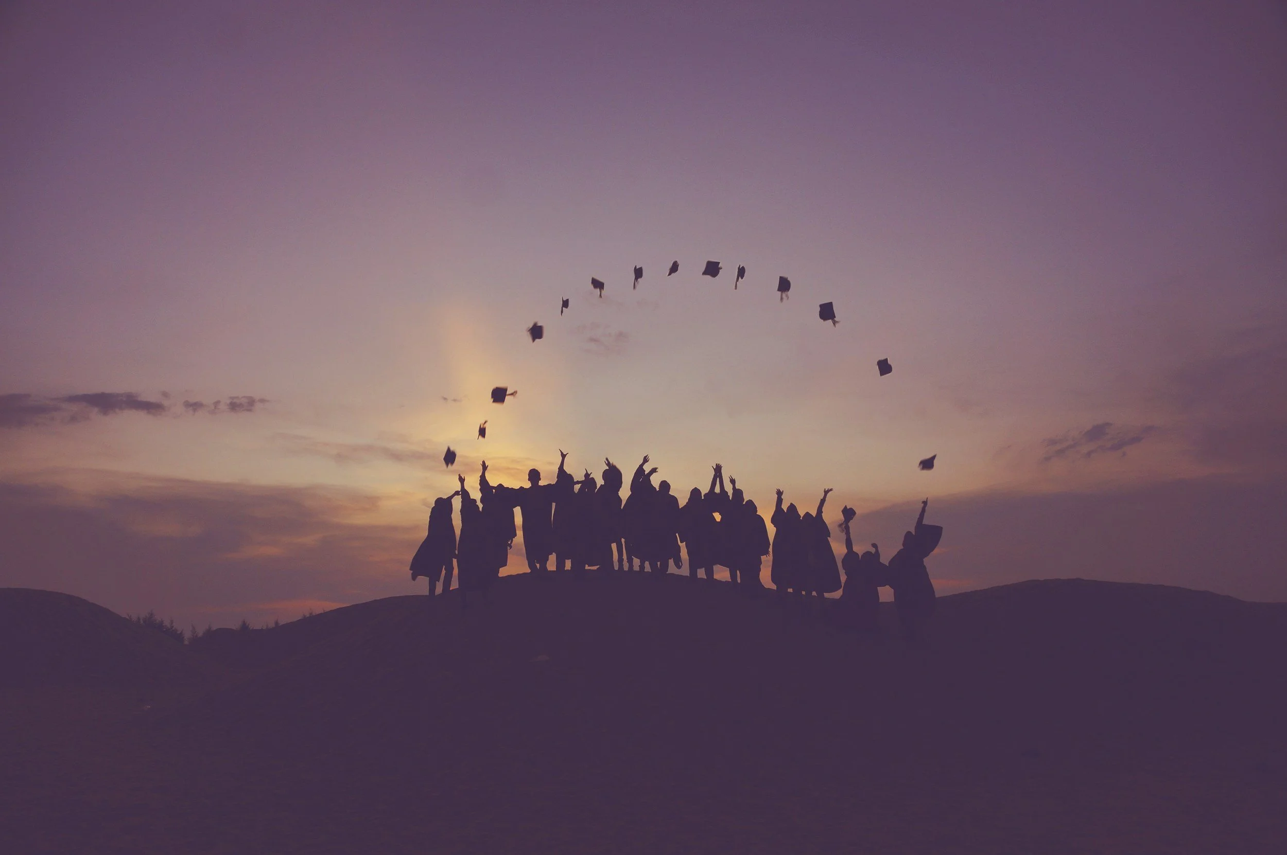 Happy graduates throwing caps into the sky during sunset celebration.