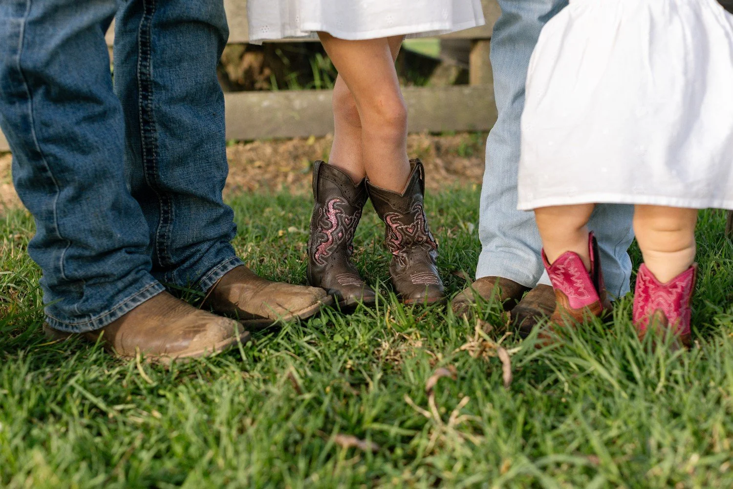 Children standing on grass, wearing cowboy boots, with only lower parts of their bodies visible.