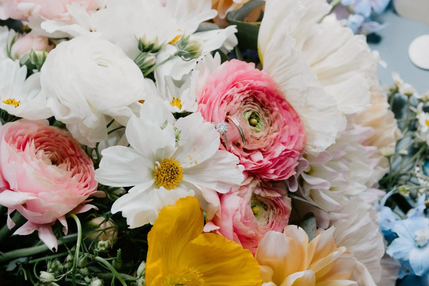 Close-up of a floral arrangement with pink, white, and yellow flowers, and wedding rings resting among the blooms.