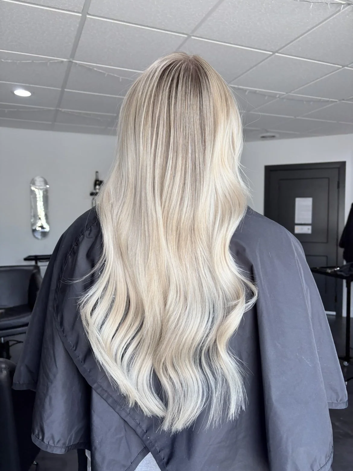 Back view of a woman with long, wavy, blonde hair in a salon or studio.