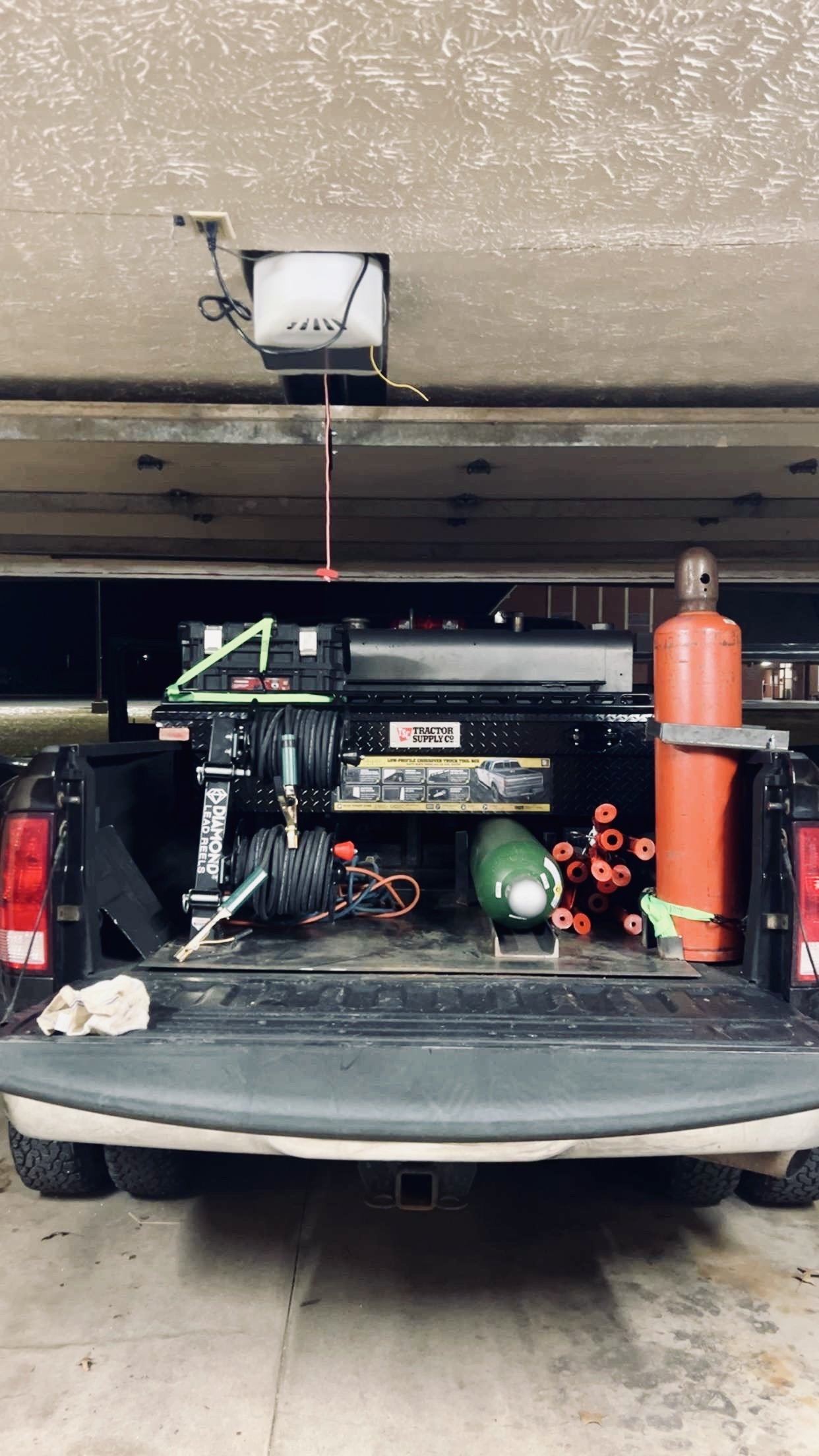 The back of a truck loaded with tools and equipment for construction or maintenance work, including hoses, a propane tank, a metal container, and an orange gas cylinder.
