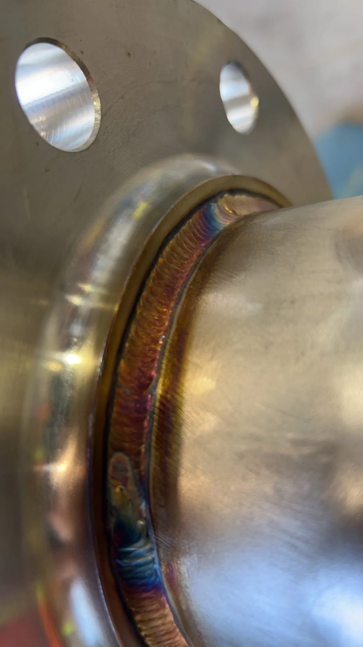 Close-up of a metallic mechanical part with welded joint showing rainbow colors.