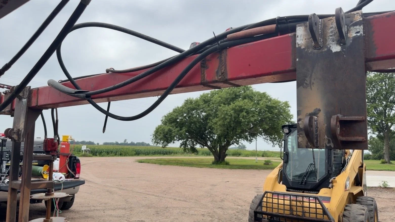 Close-up of a construction or agricultural equipment with hydraulic lines, part of a mini skid-steer loader, and equipment storage at a rural farm or field.