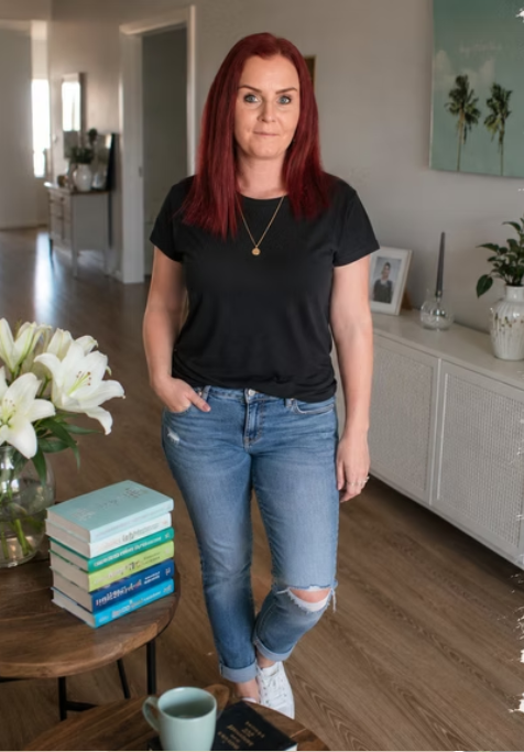 A woman with red hair wearing a black t-shirt and ripped jeans standing in a living room.