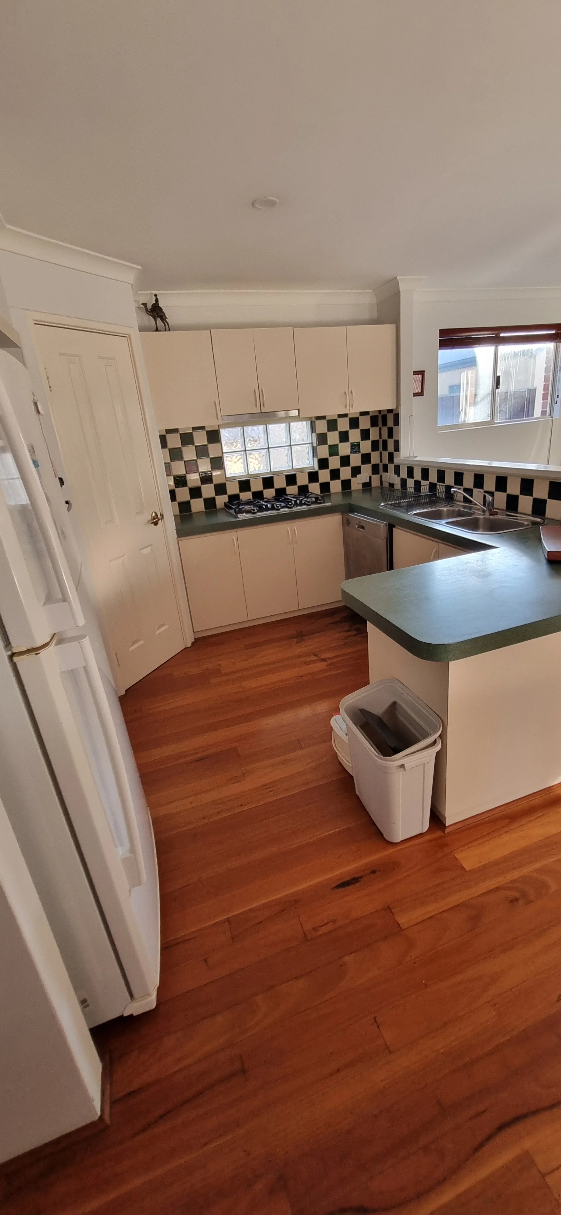 Kitchen with cream cabinets, checkered black and white backsplash, wooden flooring, and a small window above the sink.