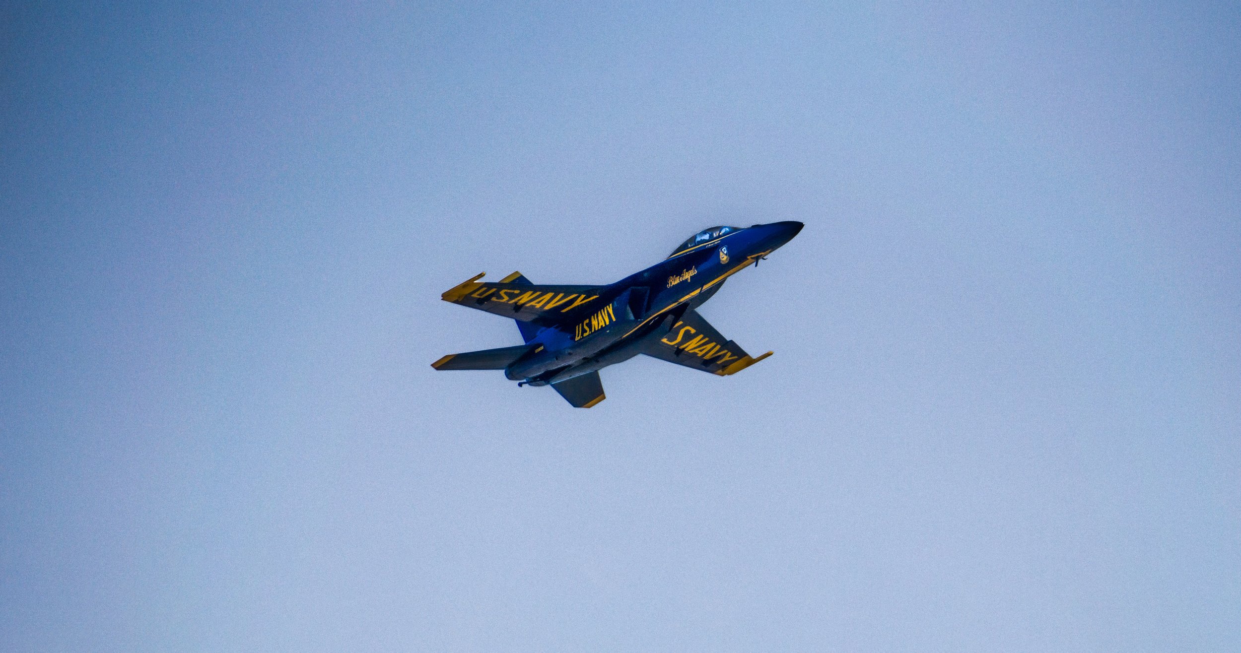 A blue and yellow U.S. Navy fighter jet flying in the sky.