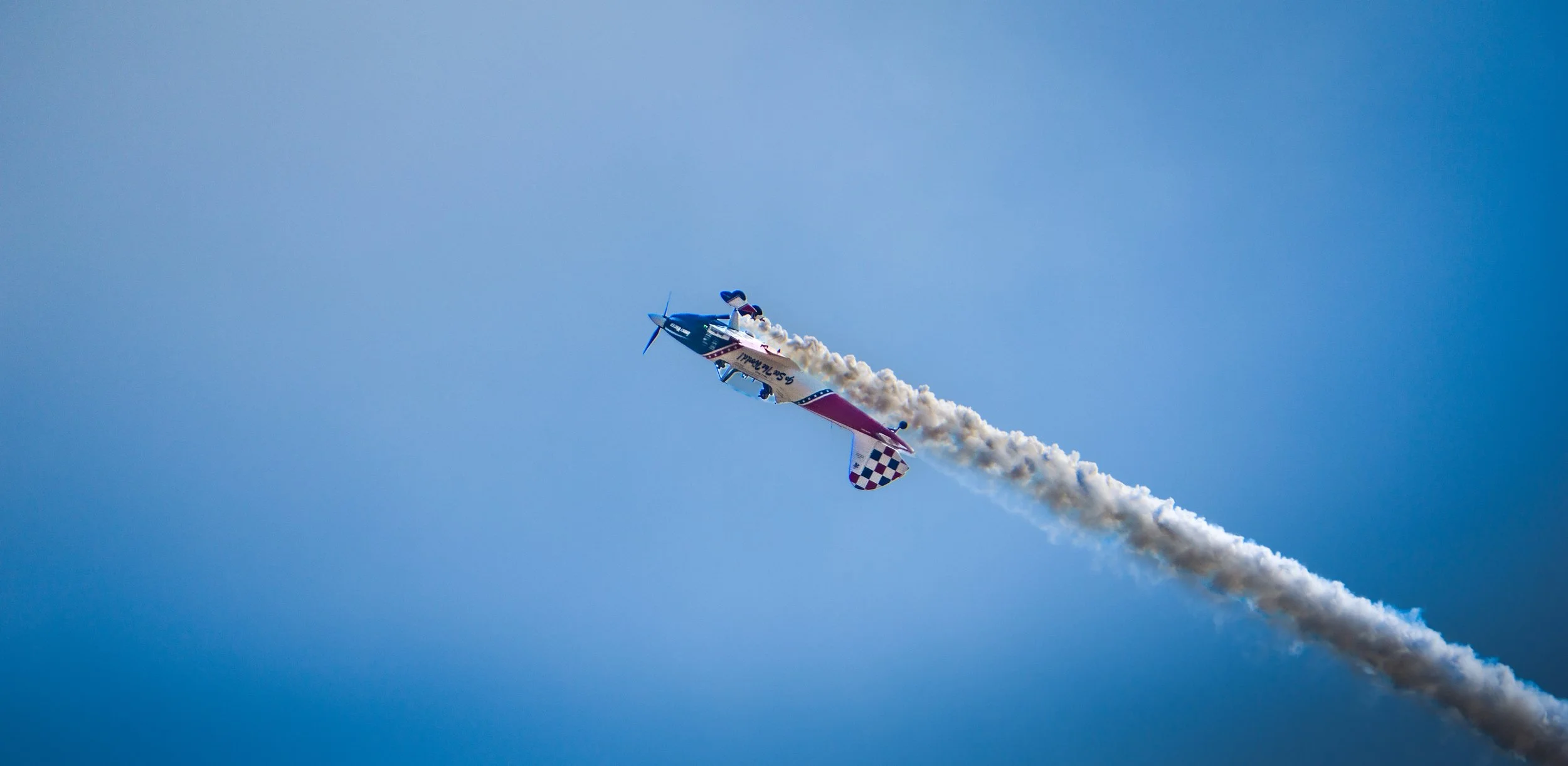 An aerobatic airplane performing a stunt in the sky, leaving a trail of white smoke behind it.