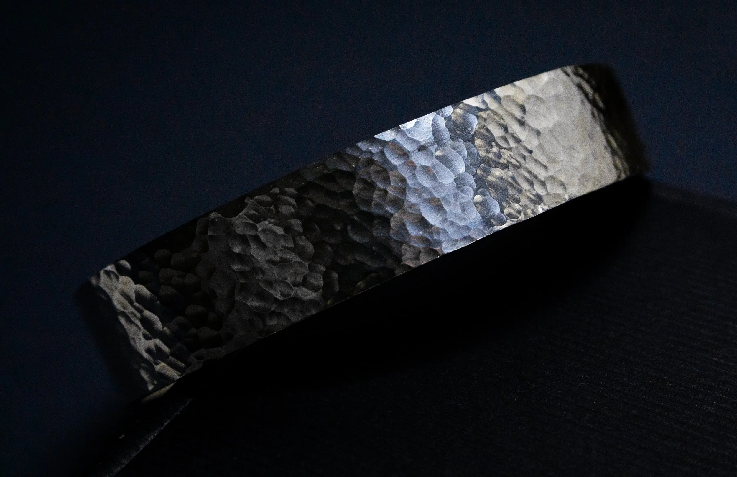 Close-up of a hammered metal surface with a textured pattern, illuminated against a dark background.