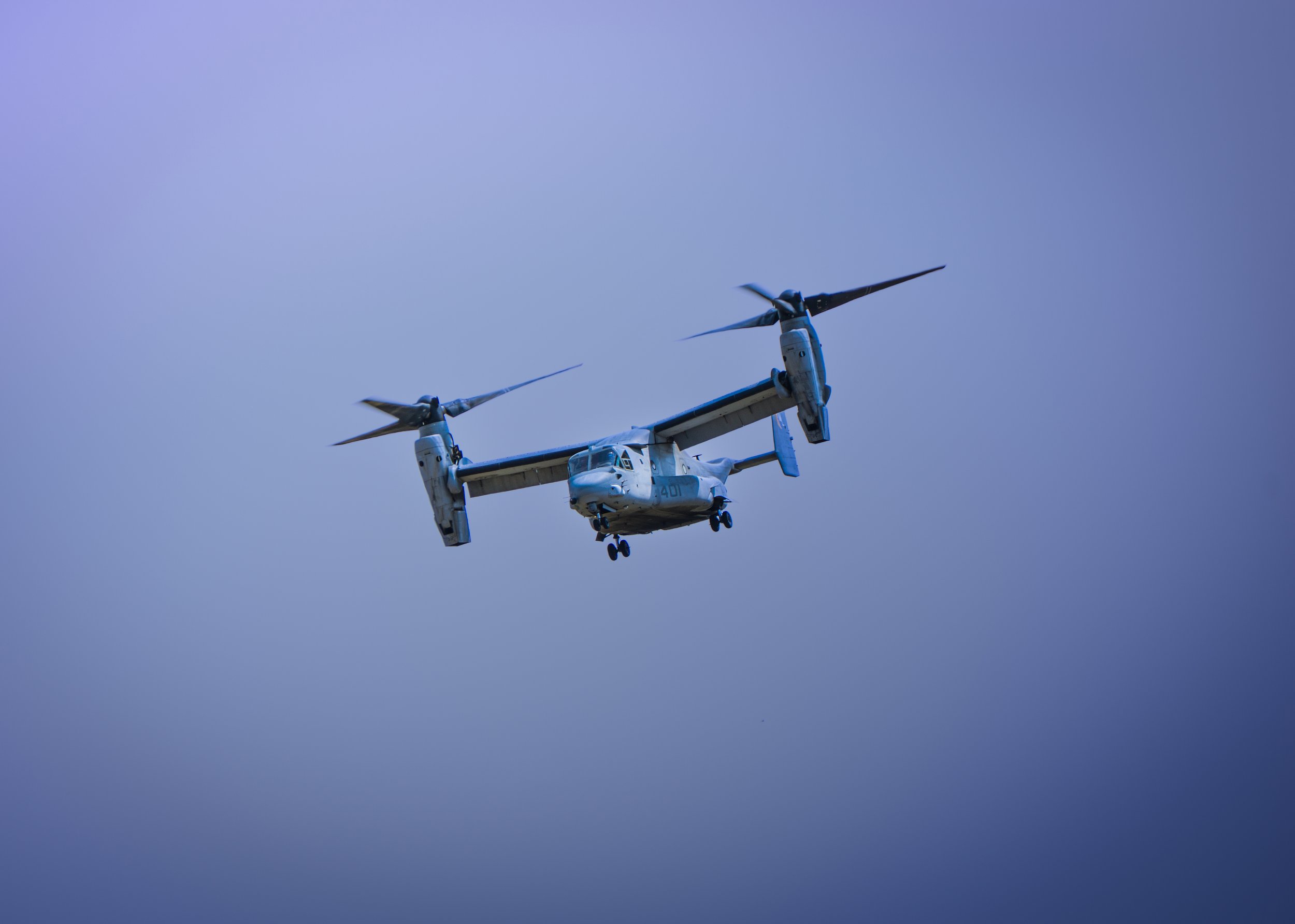 A white tiltrotor aircraft flying against a clear blue sky.