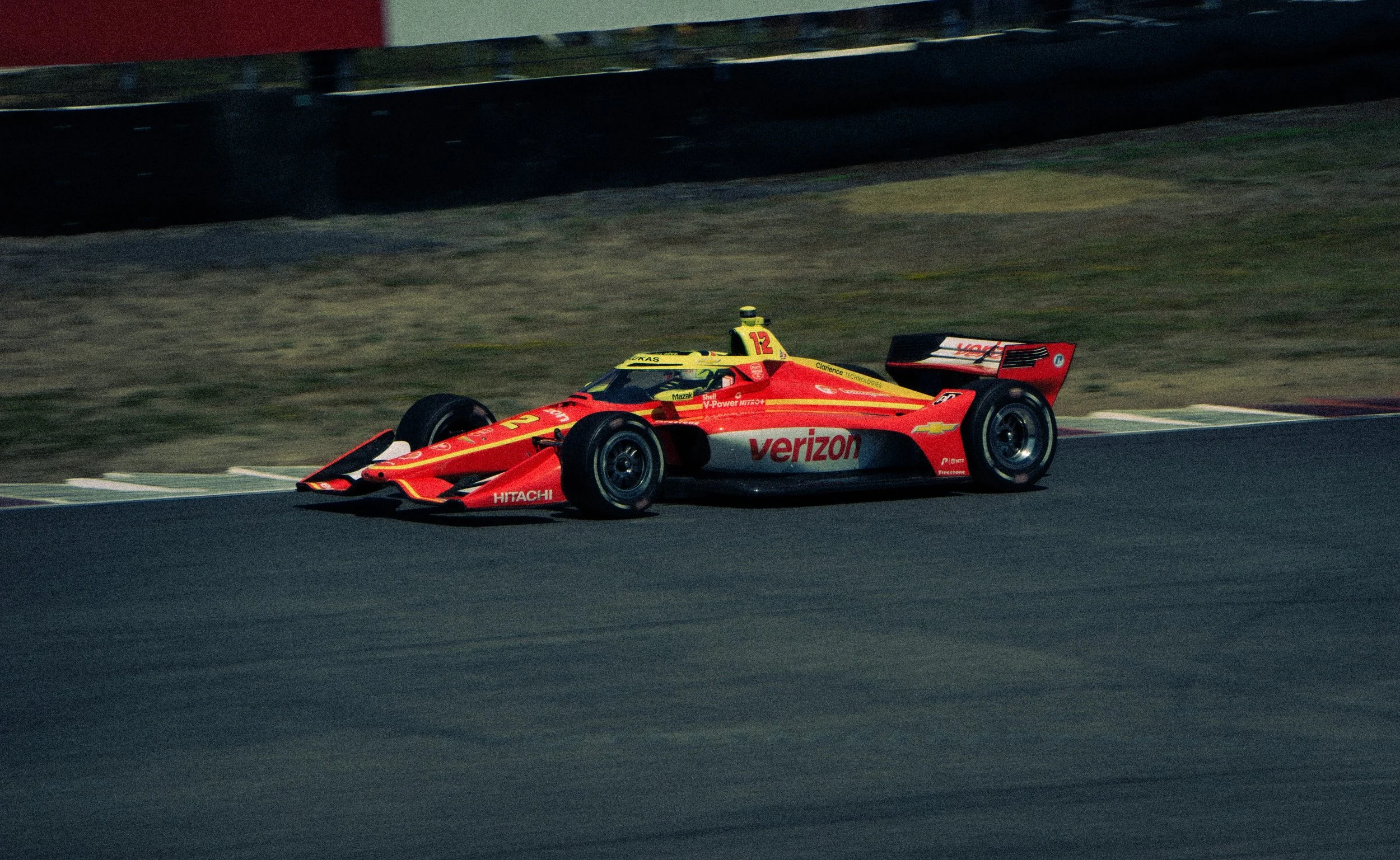 Race car with Verizon sponsorship and bright yellow and red paint driving on a racetrack.
