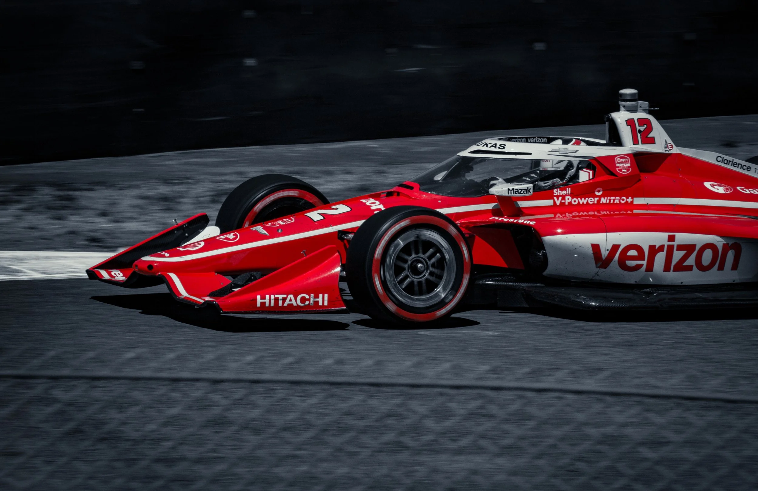 Race car with Verizon sponsorship driving on a dark racing track.