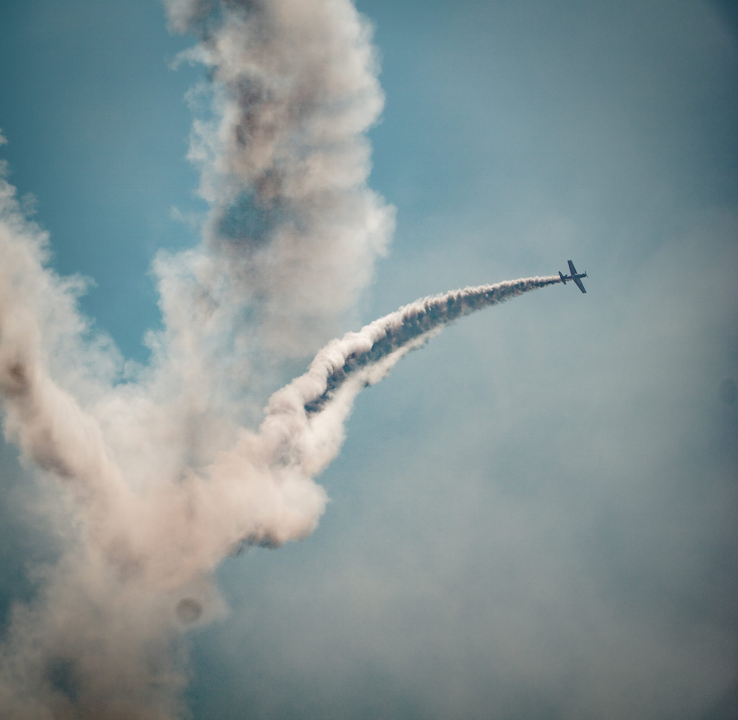 A plane performing an aerial acrobatic stunt with smoke trail in the sky.