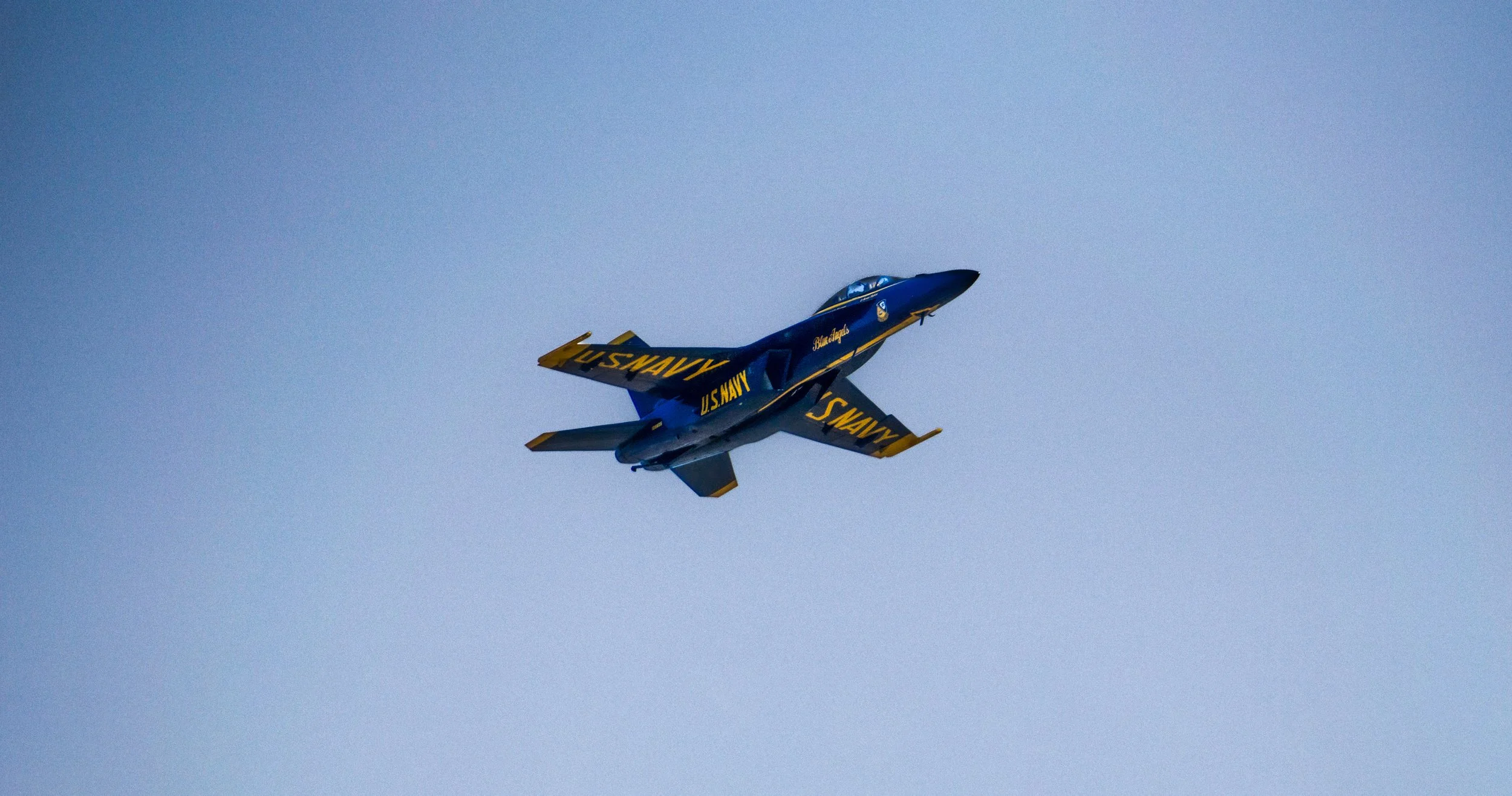 A Blue Angels fighter jet flying in a clear sky with the words U.S. NAVY on its wings.