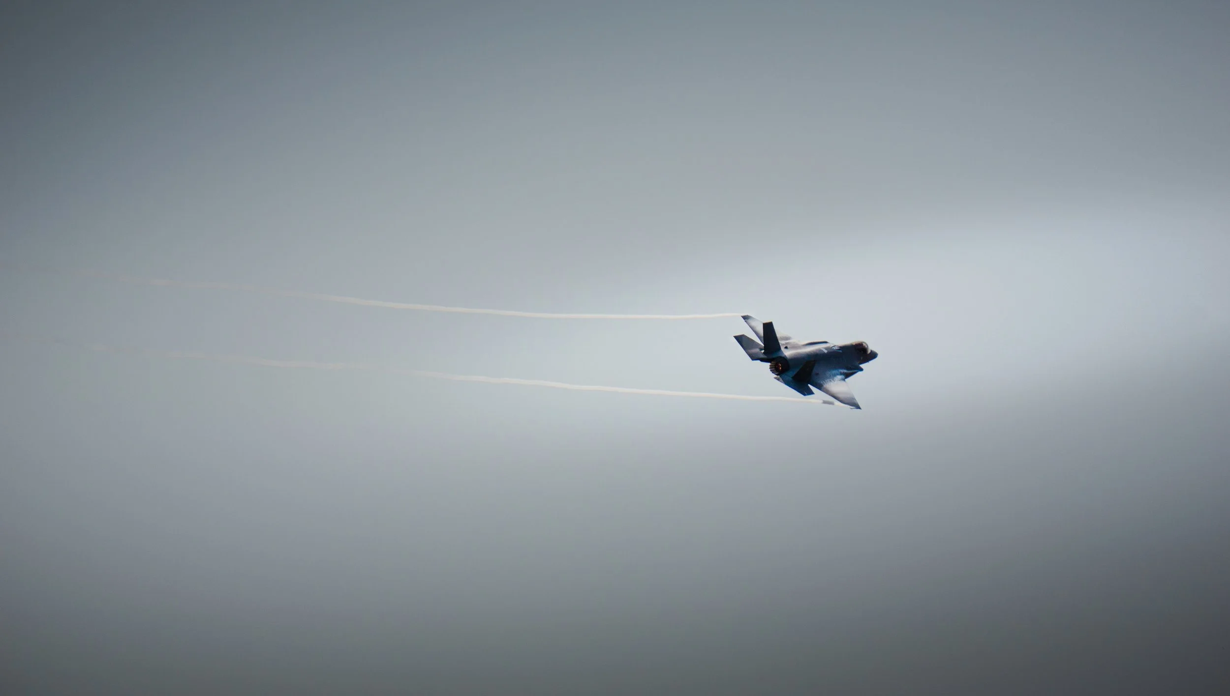 Fighter jet aircraft flying in the sky with vapor trails behind it.