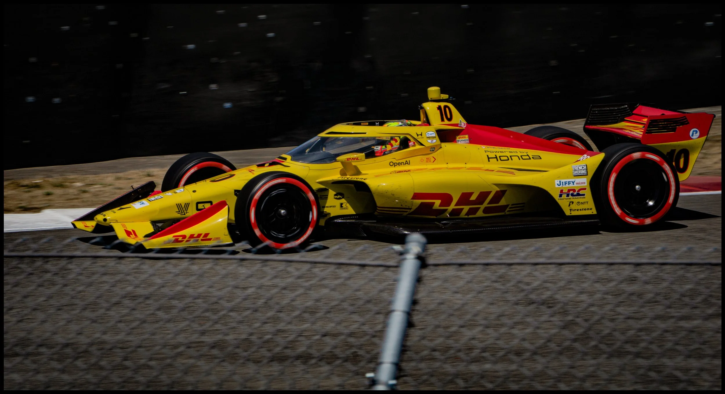 A yellow and red race car with the number 10 is driving on a race track, sponsored by DHL and Honda, during a race event.