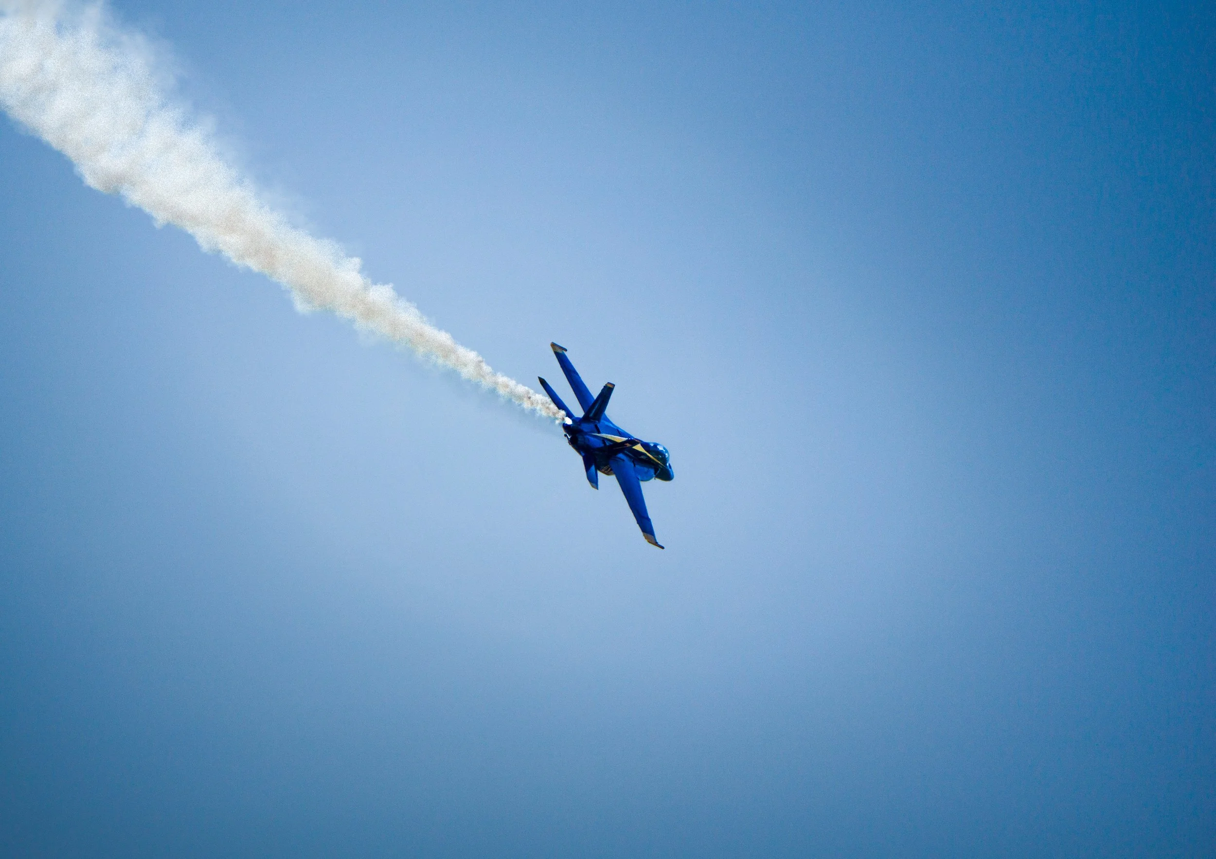 A blue fighter jet flying through the sky with white smoke trails.