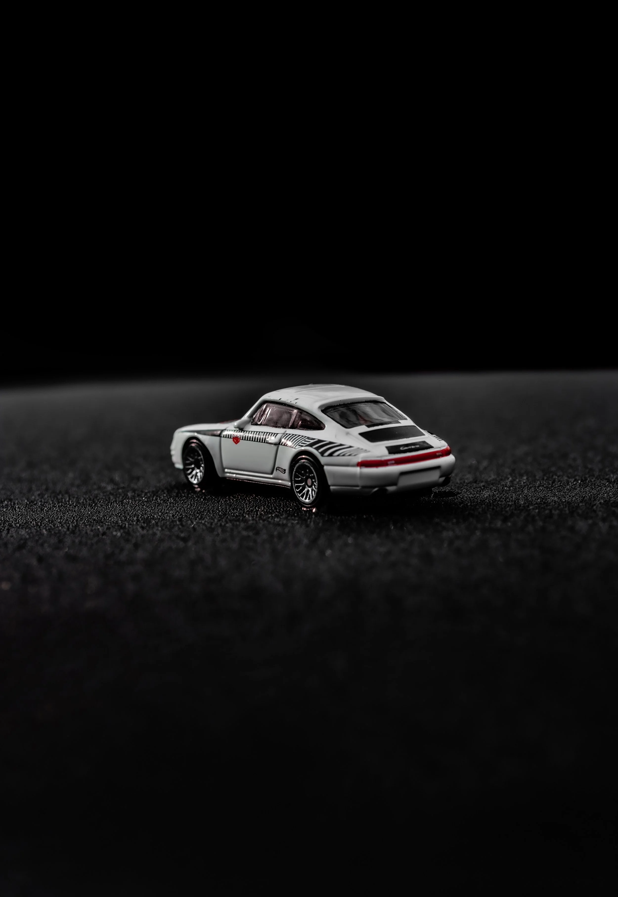 A small white toy car with black and red details is placed on a dark surface against a black background.