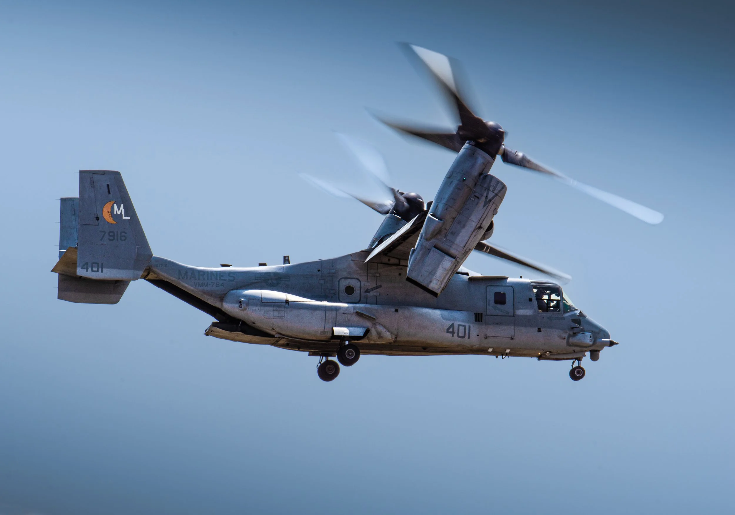 A military helicopter flying in the sky with the helicopter's rotor blades blurred due to rapid spinning.