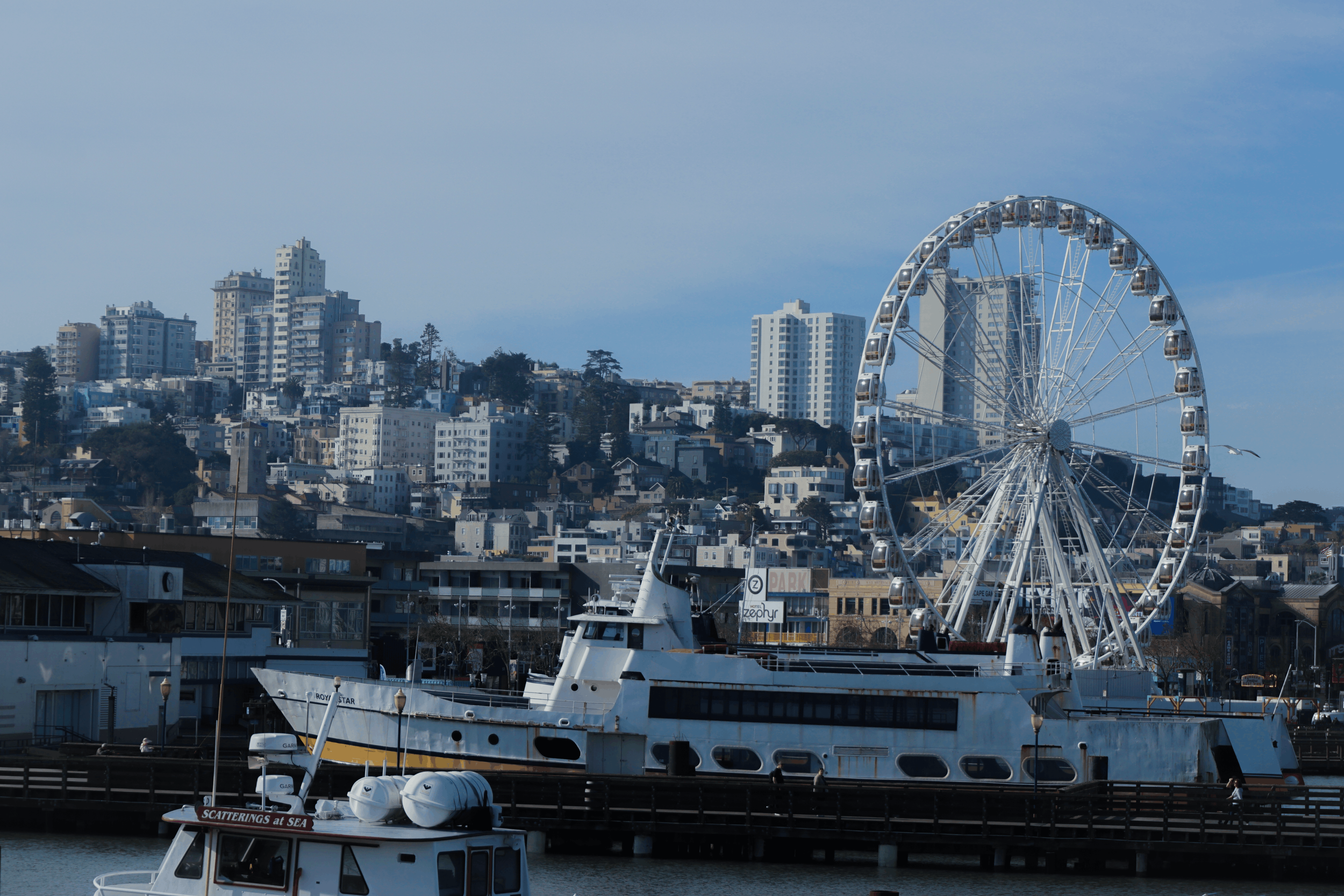 View of a cityscape with high-rise buildings, a Ferris wheel, and boats docked at a marina.