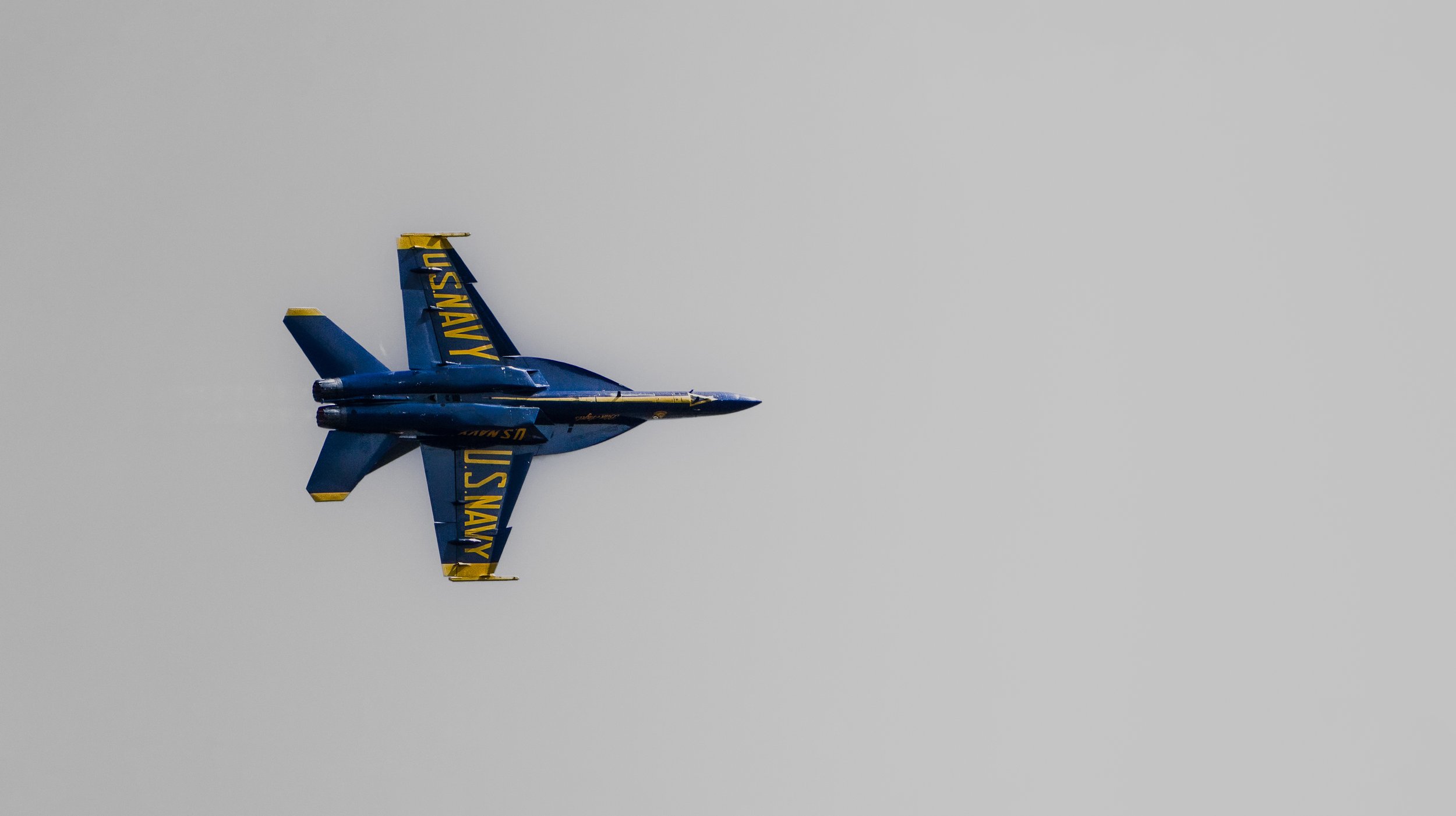 Blue and yellow U.S. Navy jet flying through gray sky.
